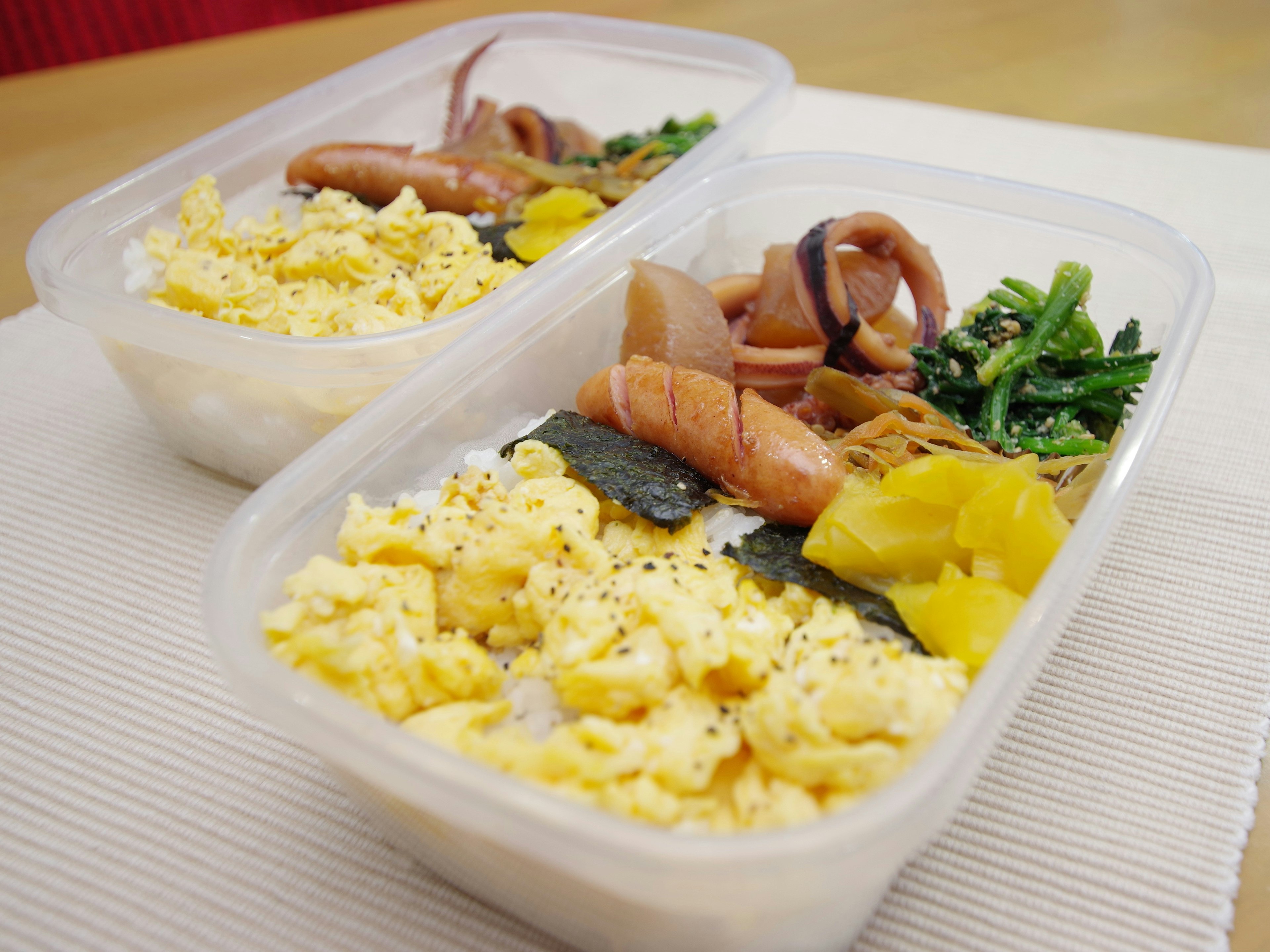 Caja de almuerzo con arroz cubierto de huevos revueltos y varios acompañamientos