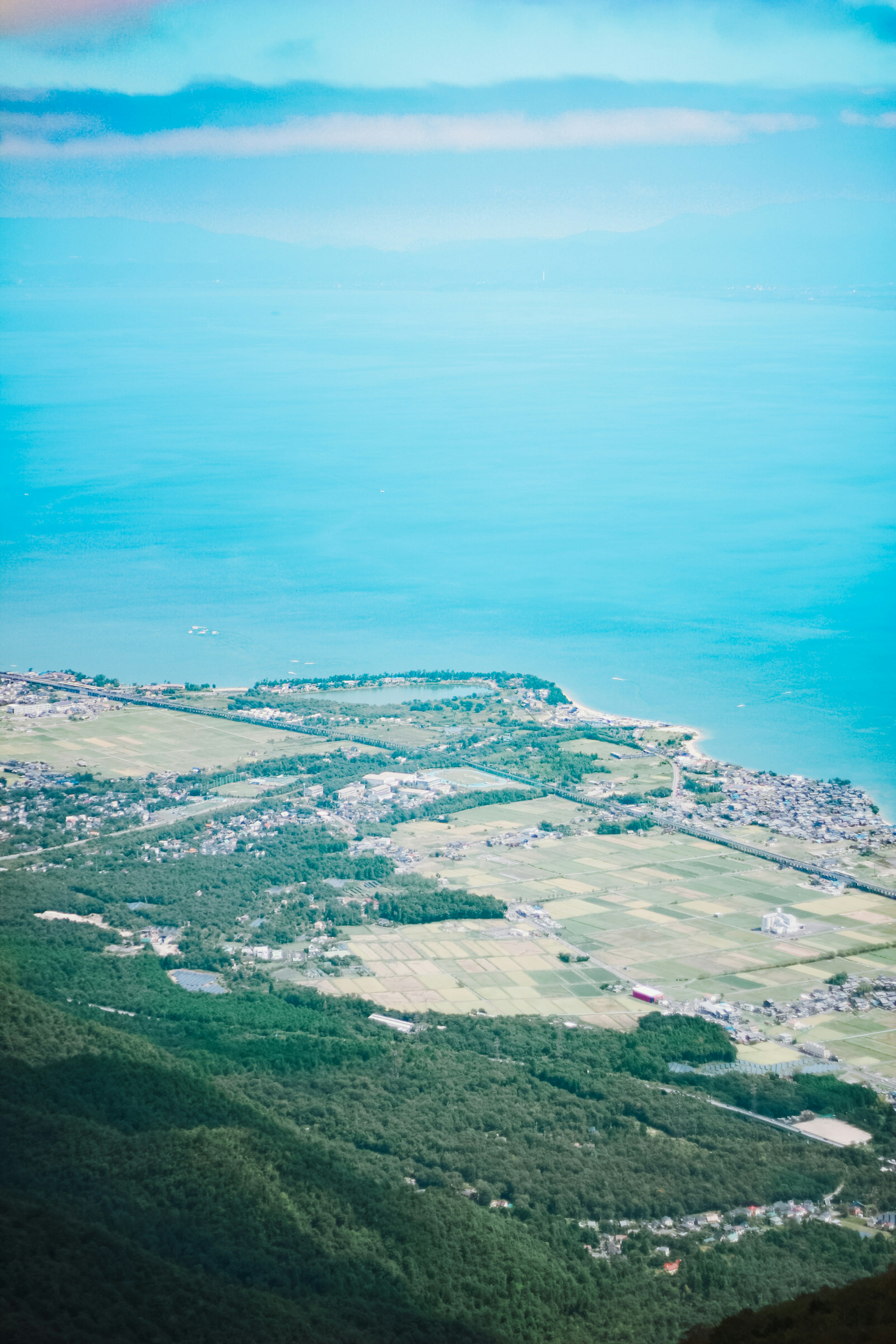 Vue aérienne de l'océan bleu et des collines vertes avec un village côtier sous un ciel clair