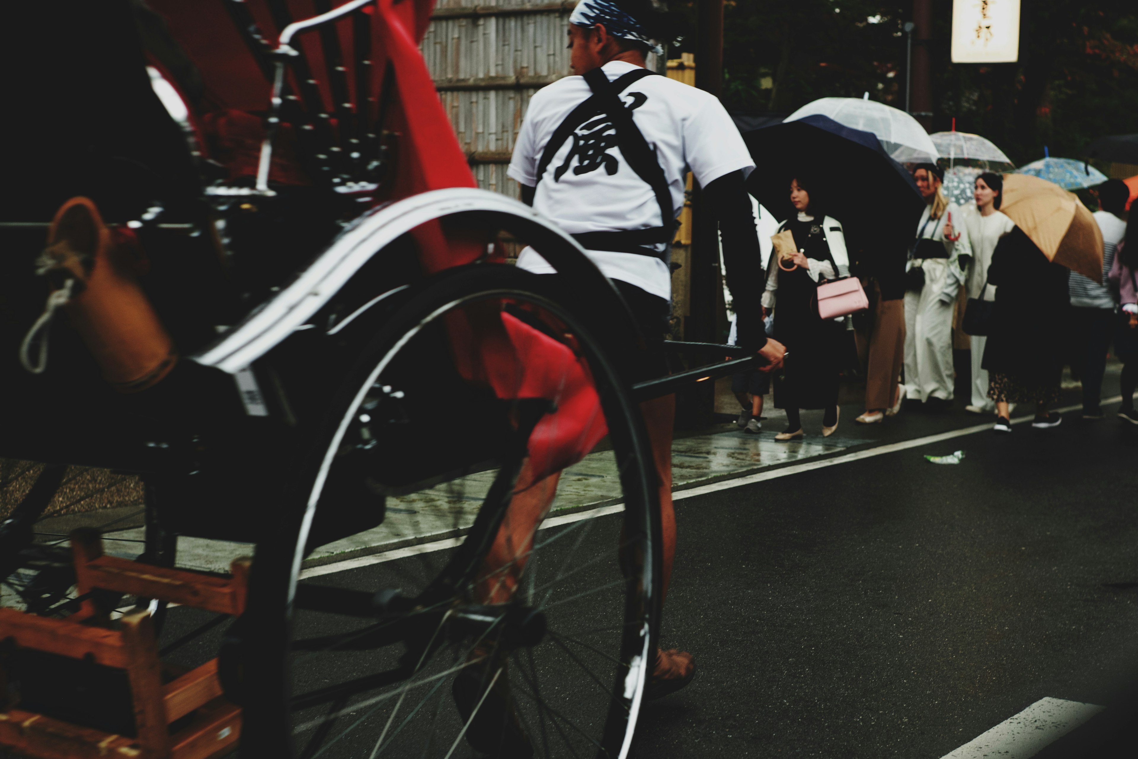 Un homme tirant une rickshaw avec une file de personnes tenant des parapluies