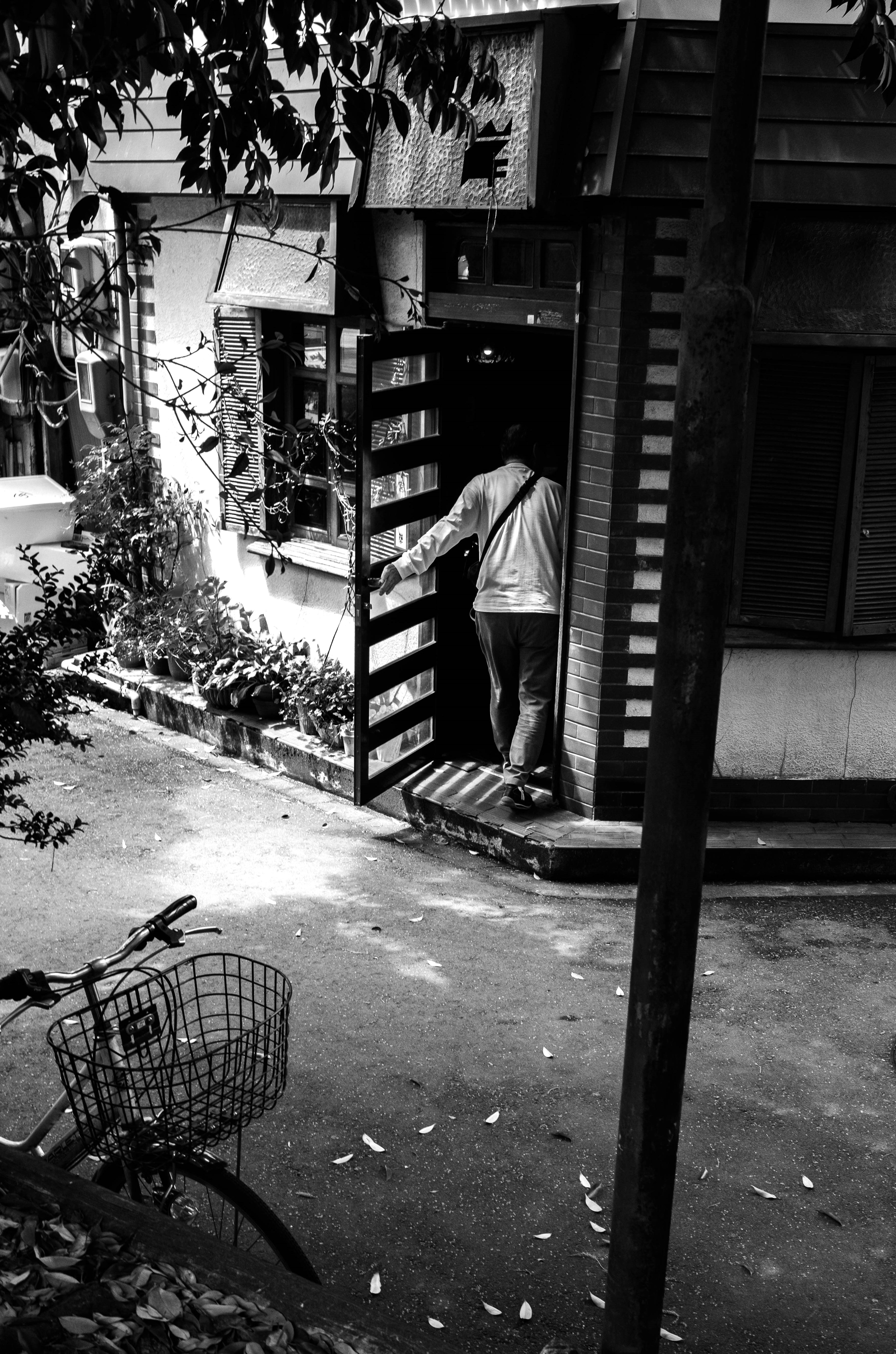 Photo en noir et blanc d'une personne sortant d'une maison avec un vélo à proximité