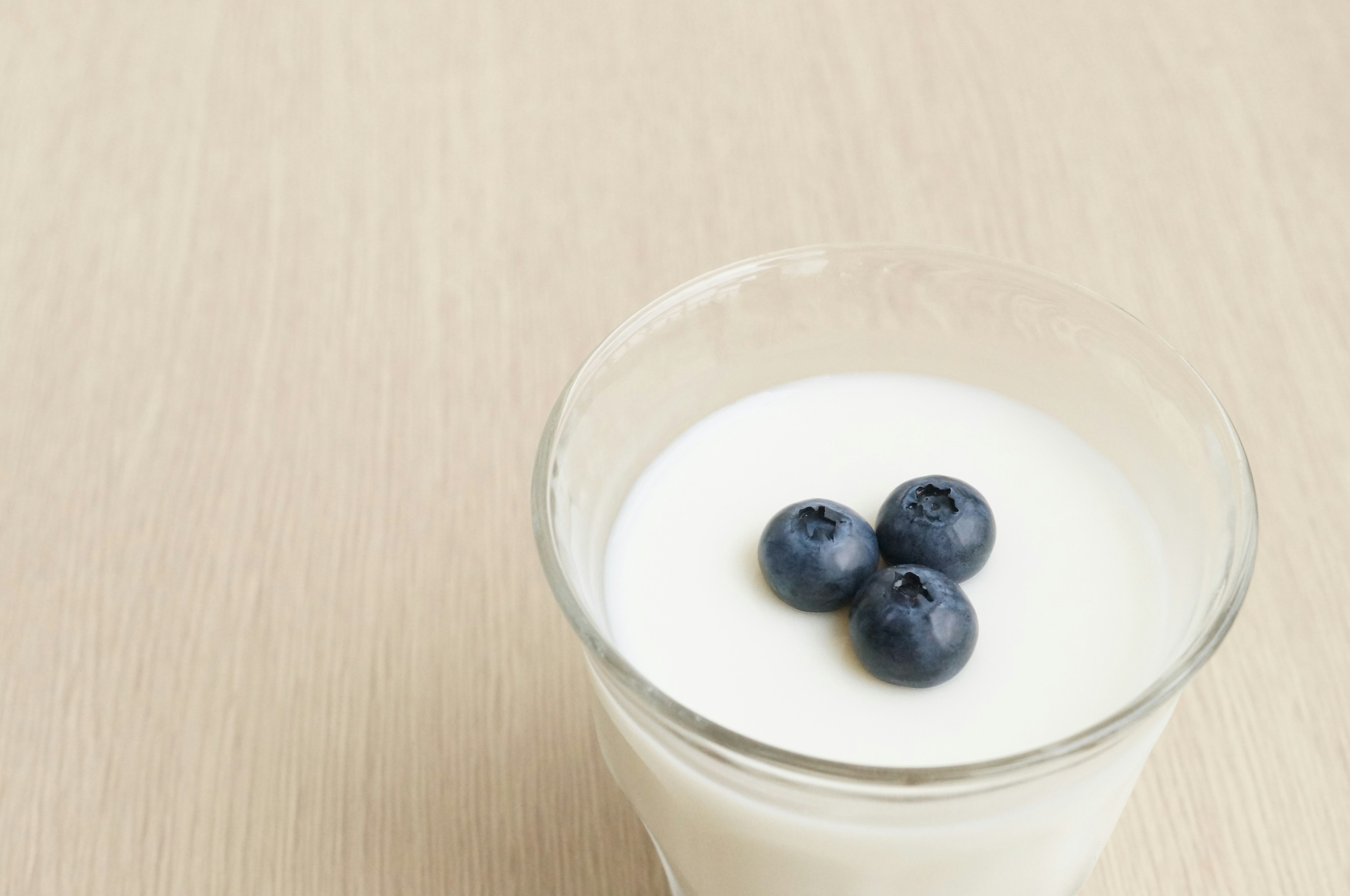 A clear glass containing yogurt topped with three blueberries