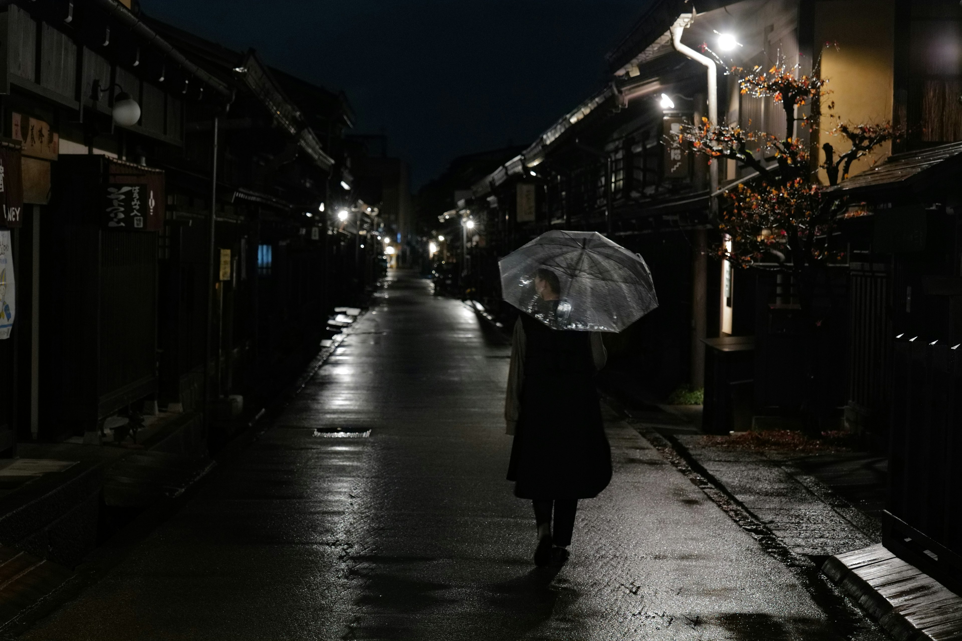 A person walking with an umbrella in a nighttime street scene