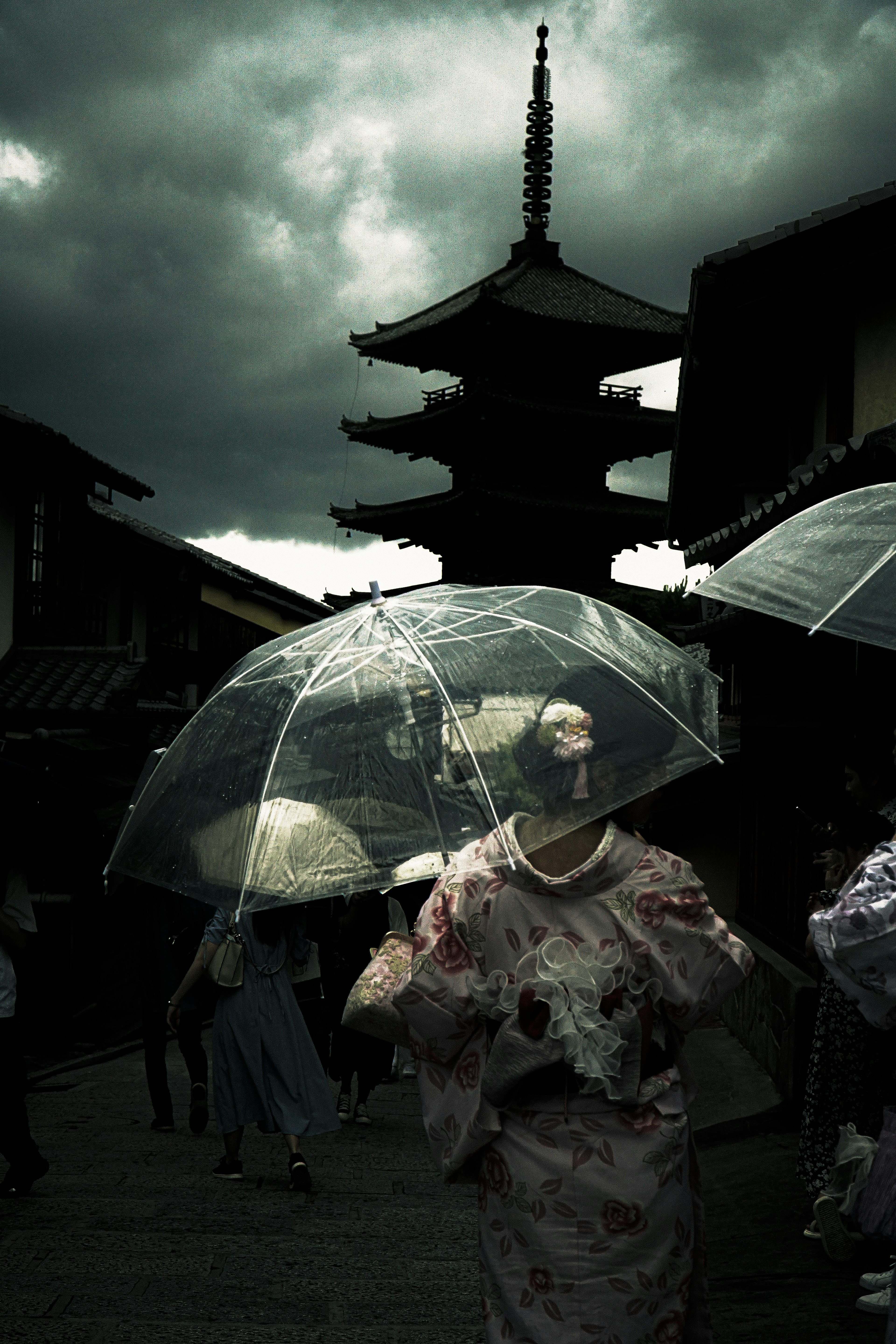 Femme en kimono tenant un parapluie transparent sous un ciel sombre avec une pagode traditionnelle