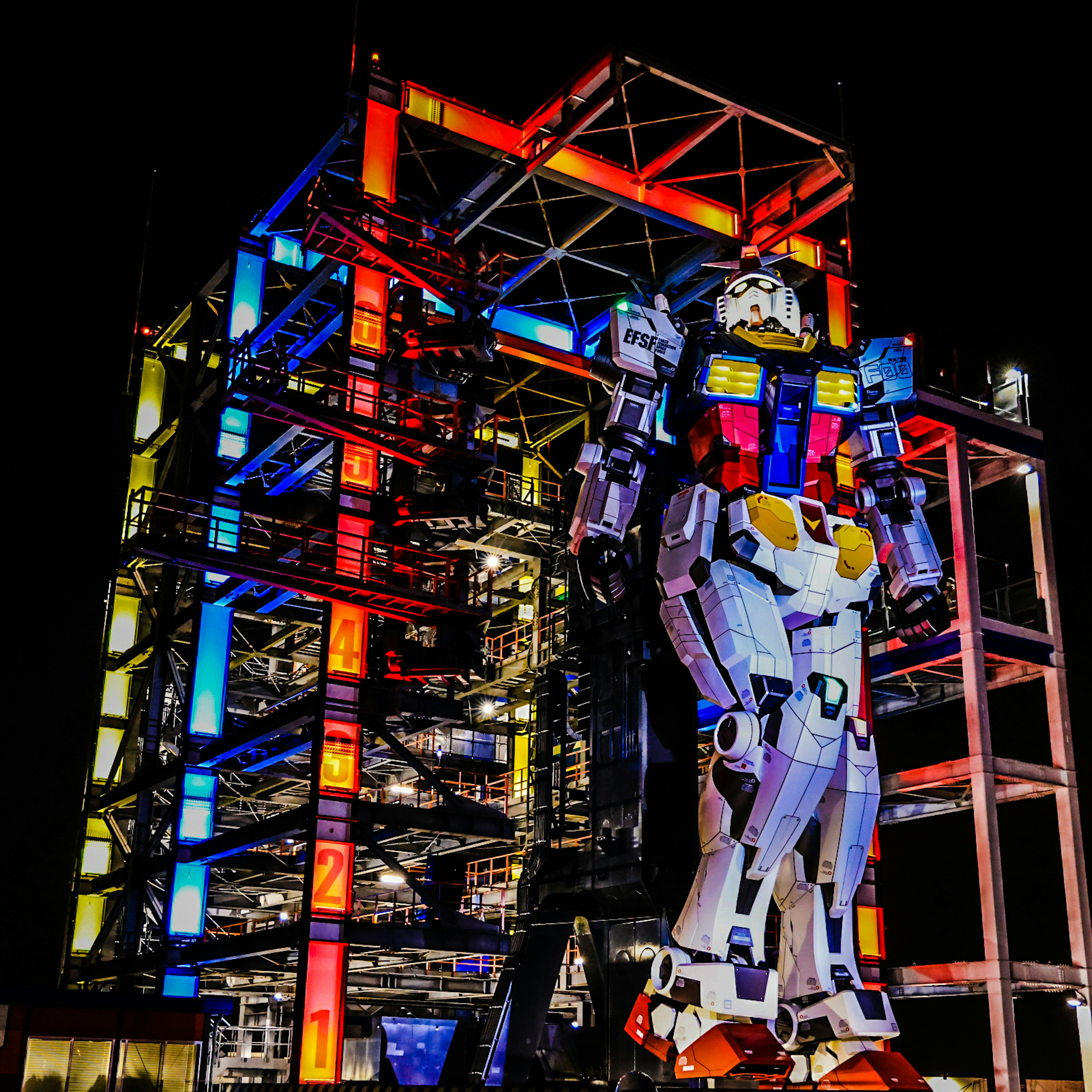 Riesen-Gundam-Roboter mit bunten Lichtern bei Nacht vor einer modernen Struktur