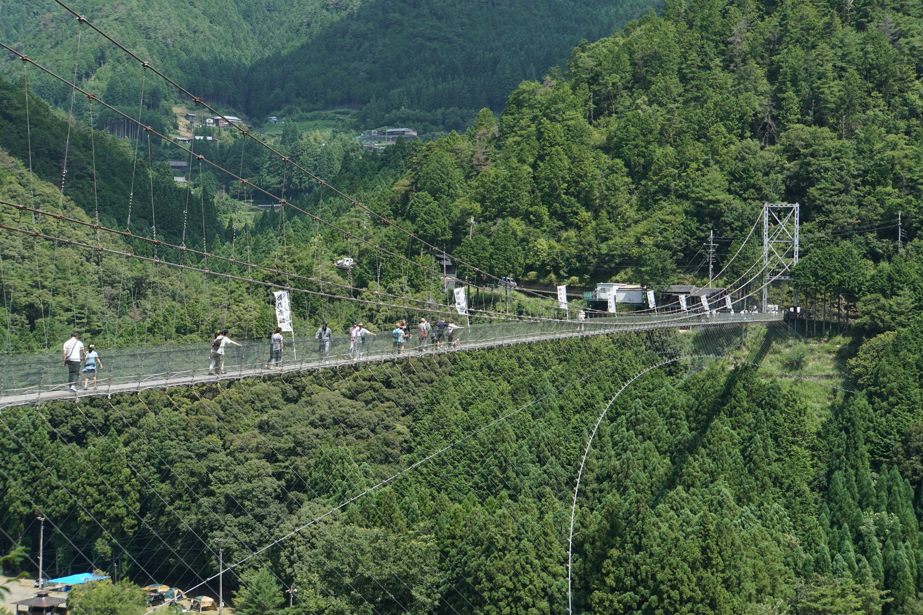 Menschen, die eine Hängebrücke überqueren, umgeben von grünen Bergen