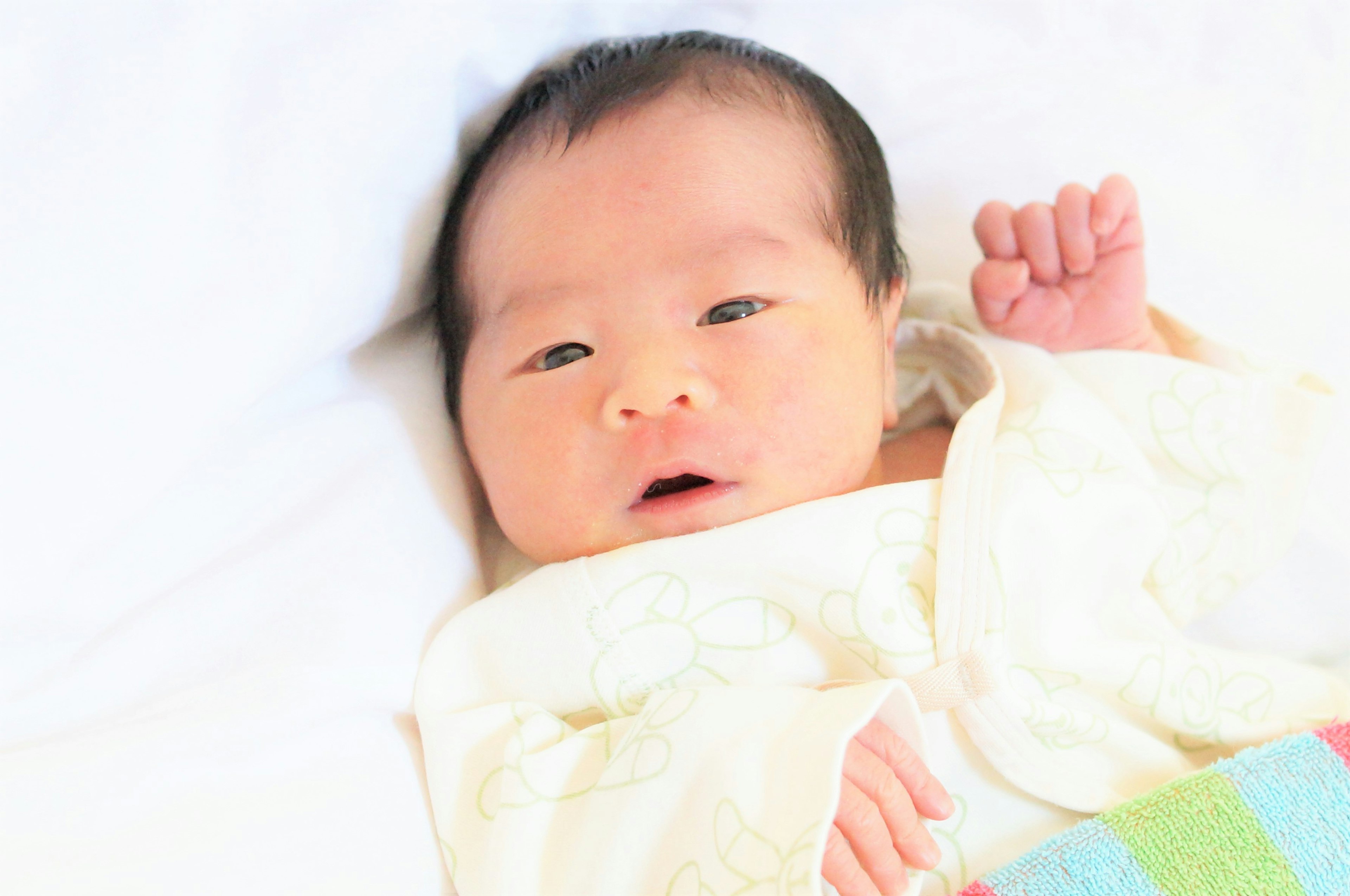 Baby liegt auf einer weißen Decke mit einer bunten Decke