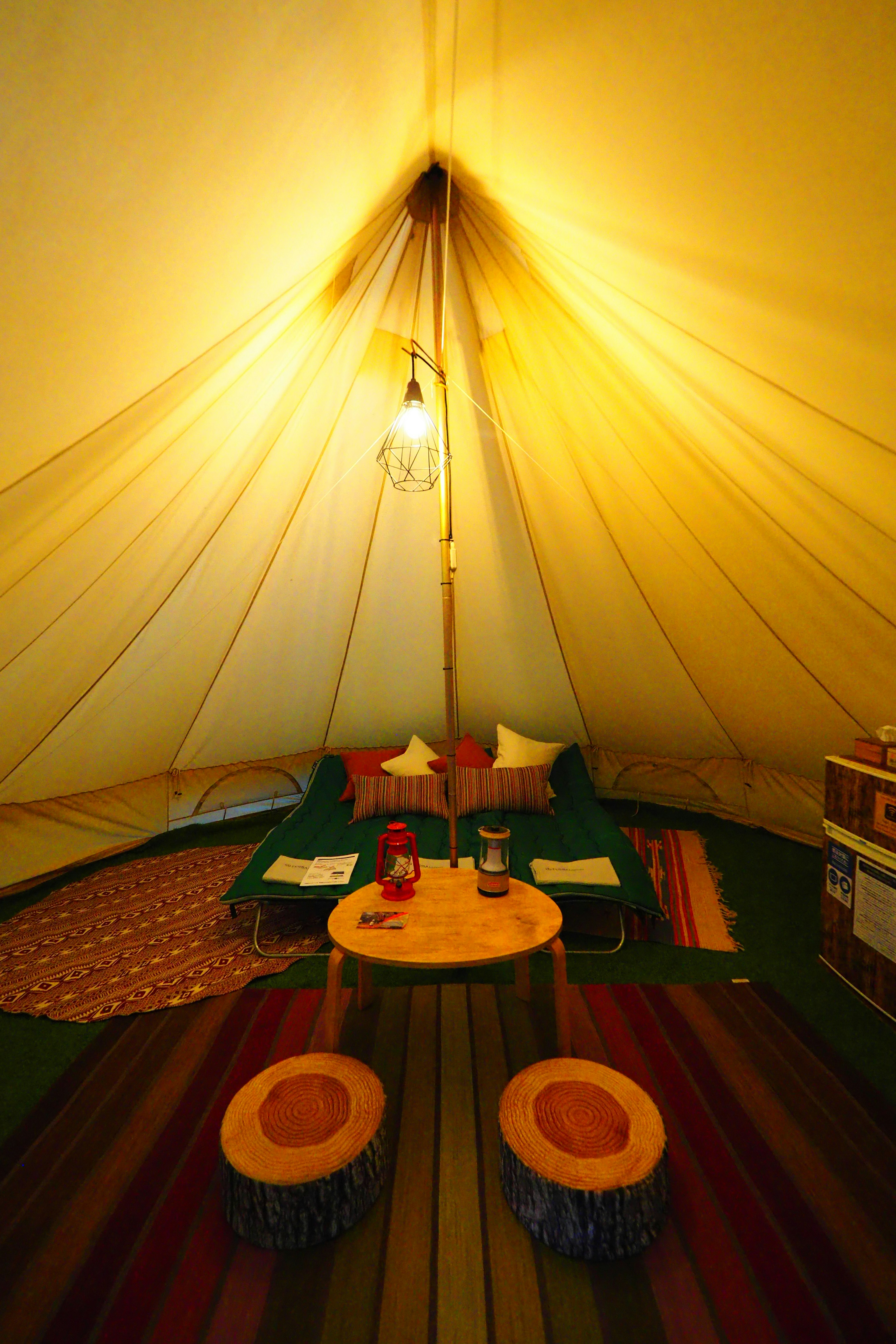 Interior of a tent featuring colorful cushions and a round table with hanging light