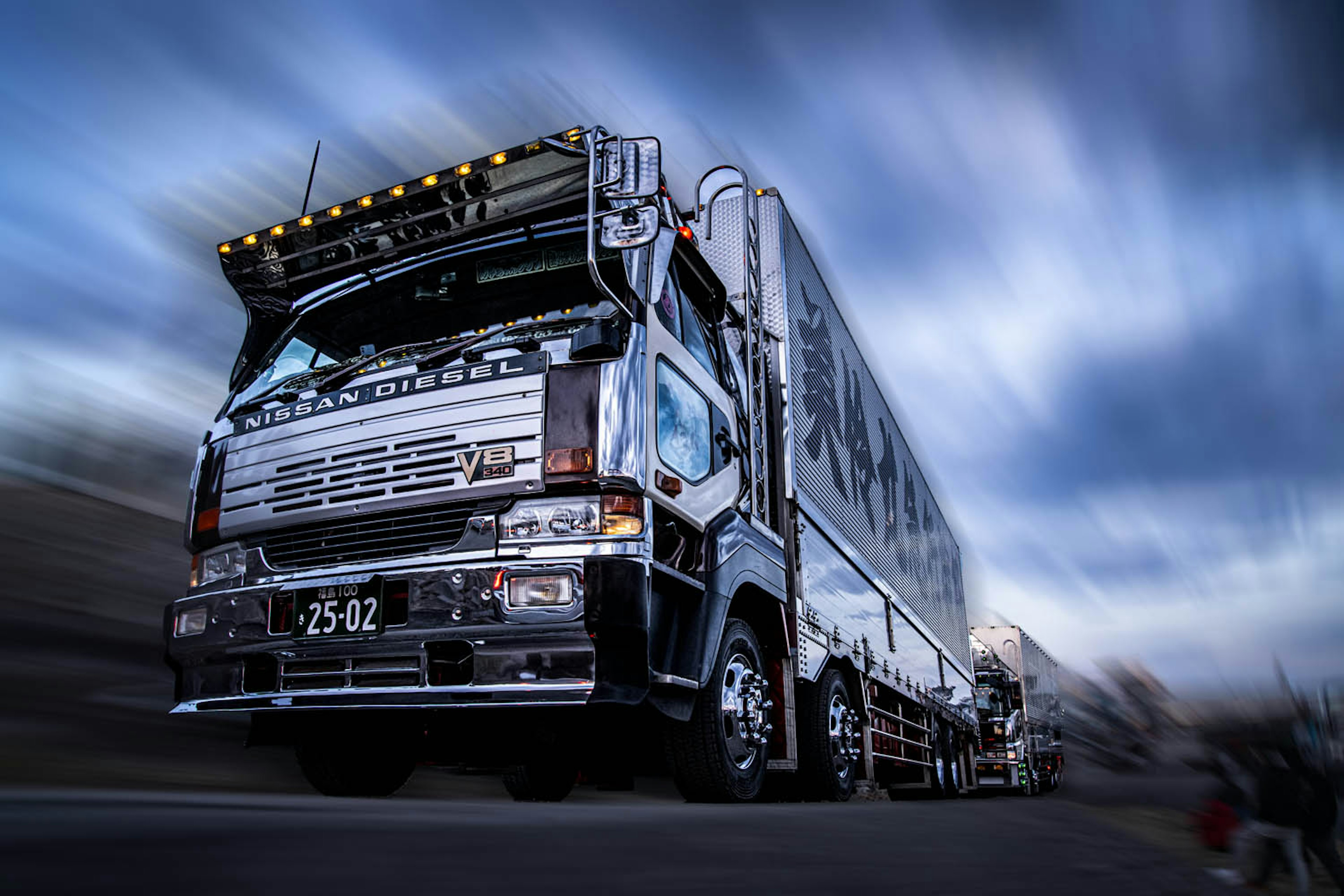 Un camion nero che guida su una strada con nuvole blu e bianche nel cielo