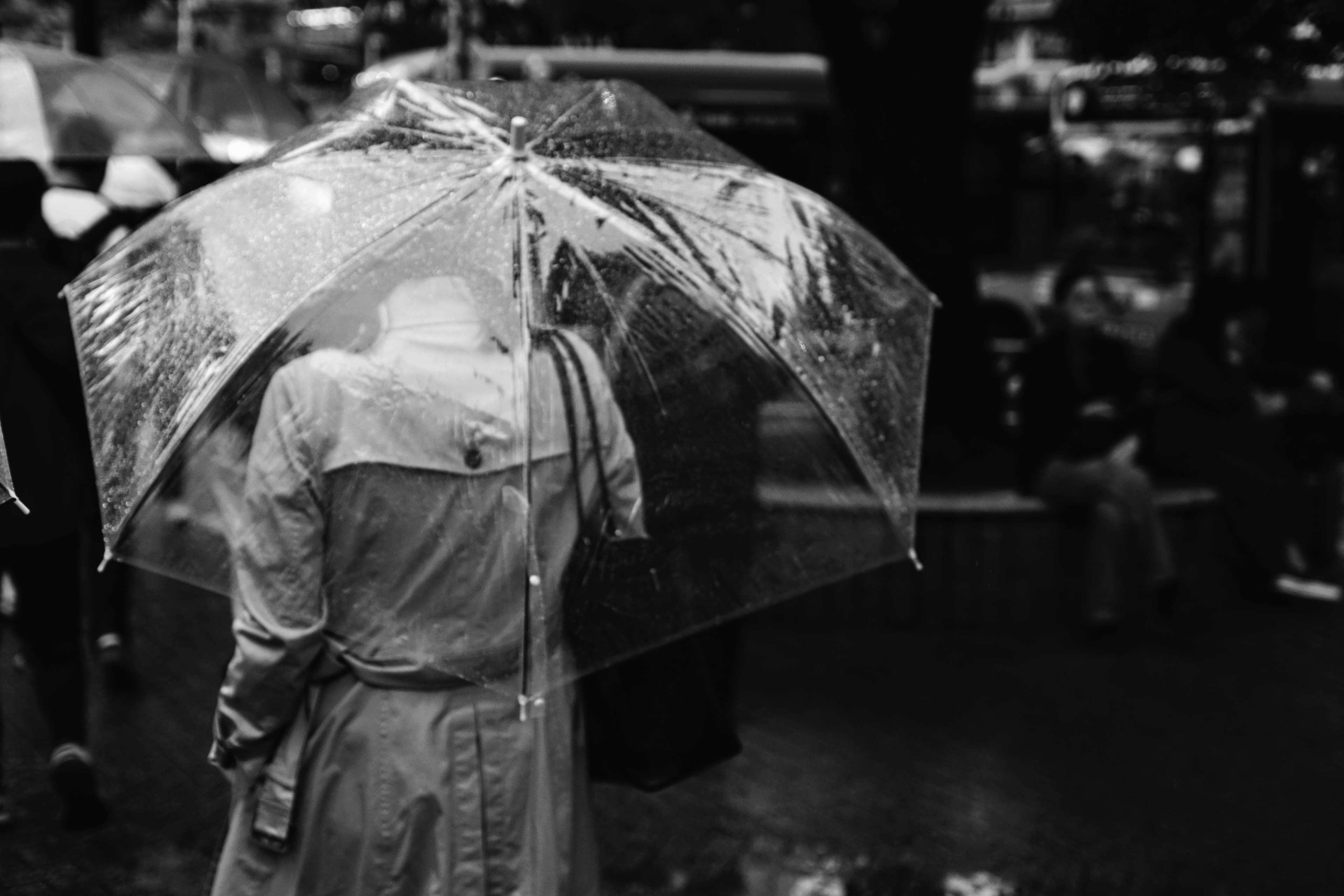 Une personne tenant un parapluie transparent marchant sous la pluie en noir et blanc