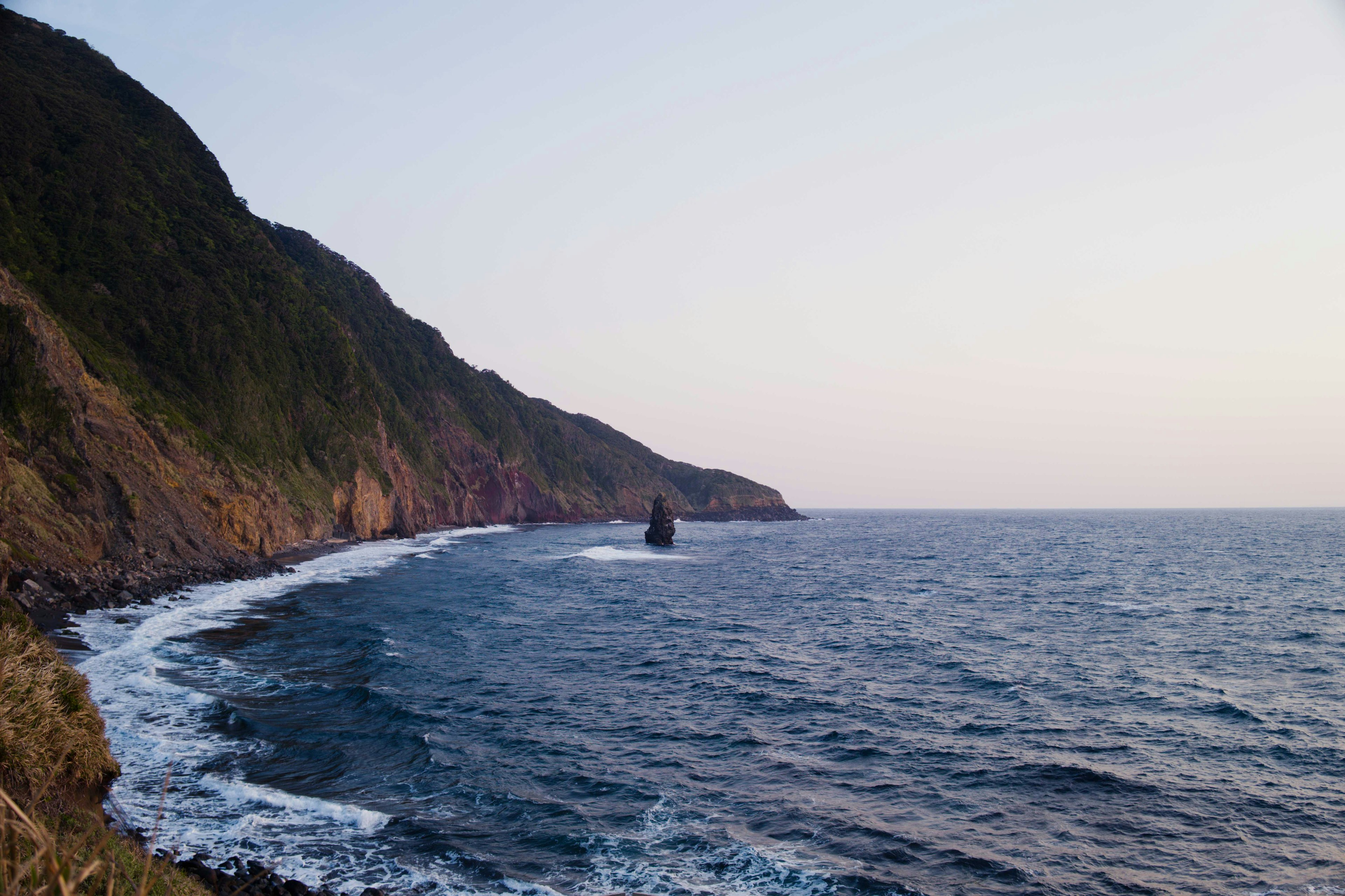 Coastal landscape featuring waves and a rocky shoreline during sunset