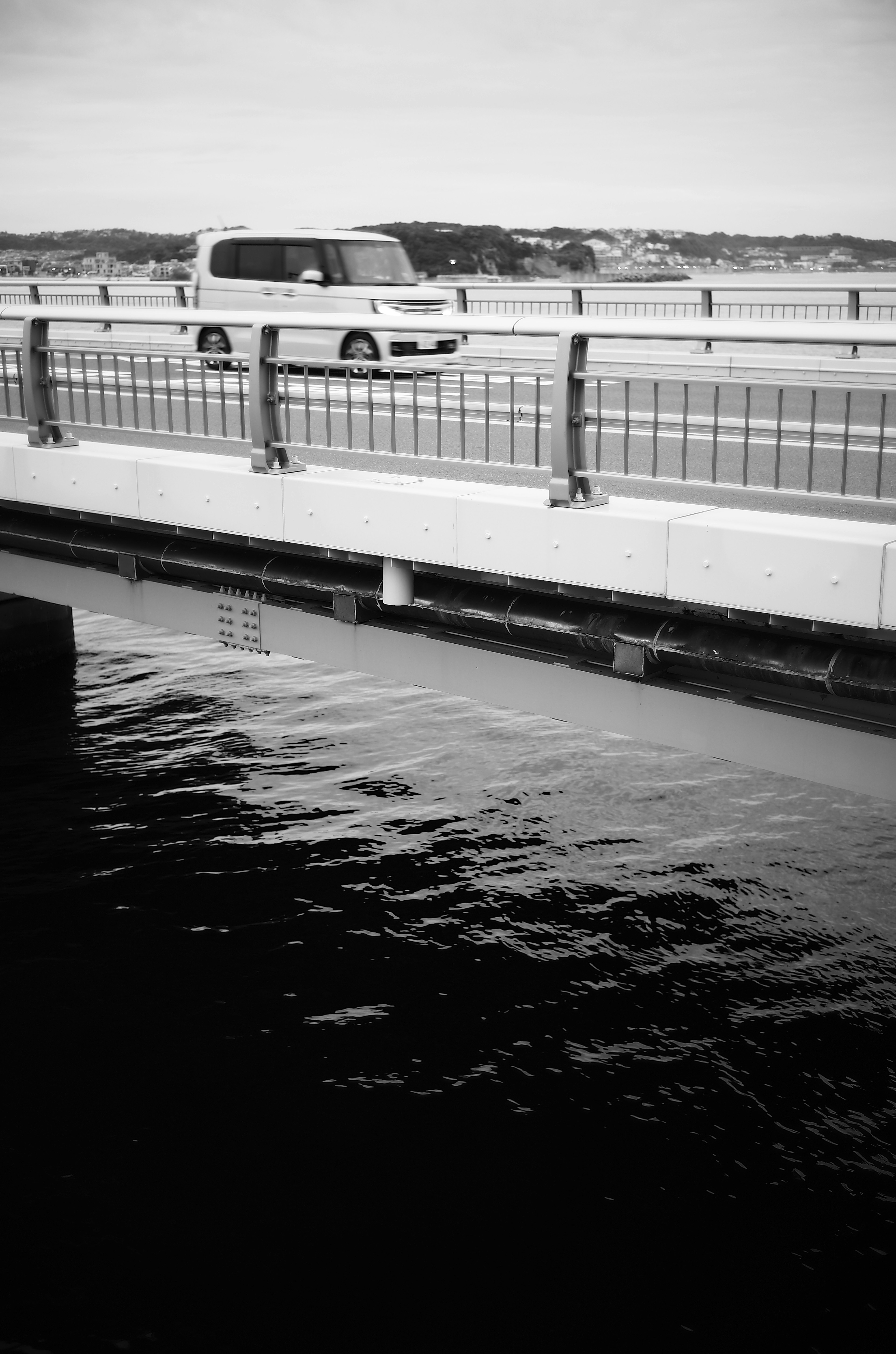 Imagen en blanco y negro de un puente con agua fluyendo y un coche