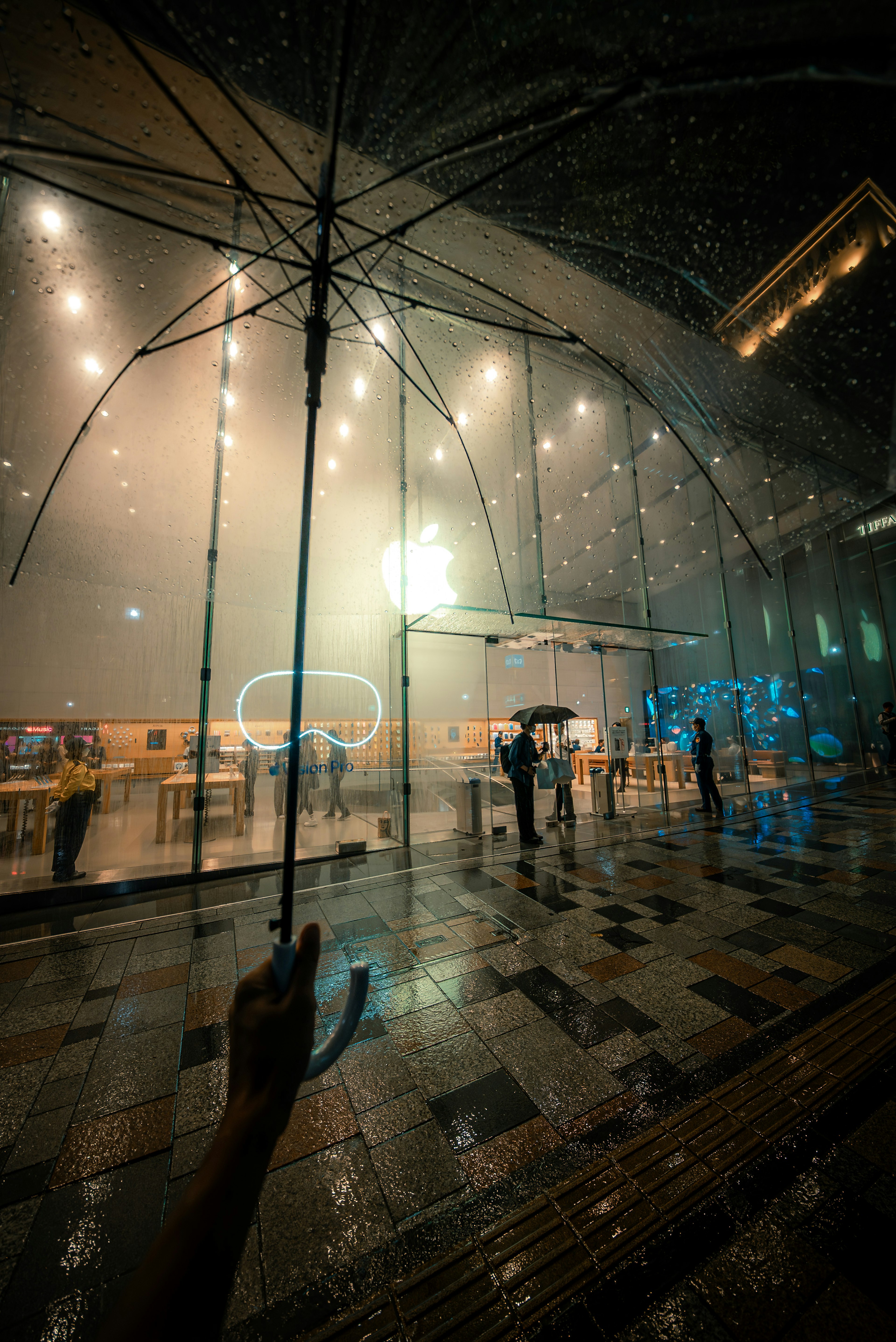 雨の中で傘を持つ人々と明るい店の前景