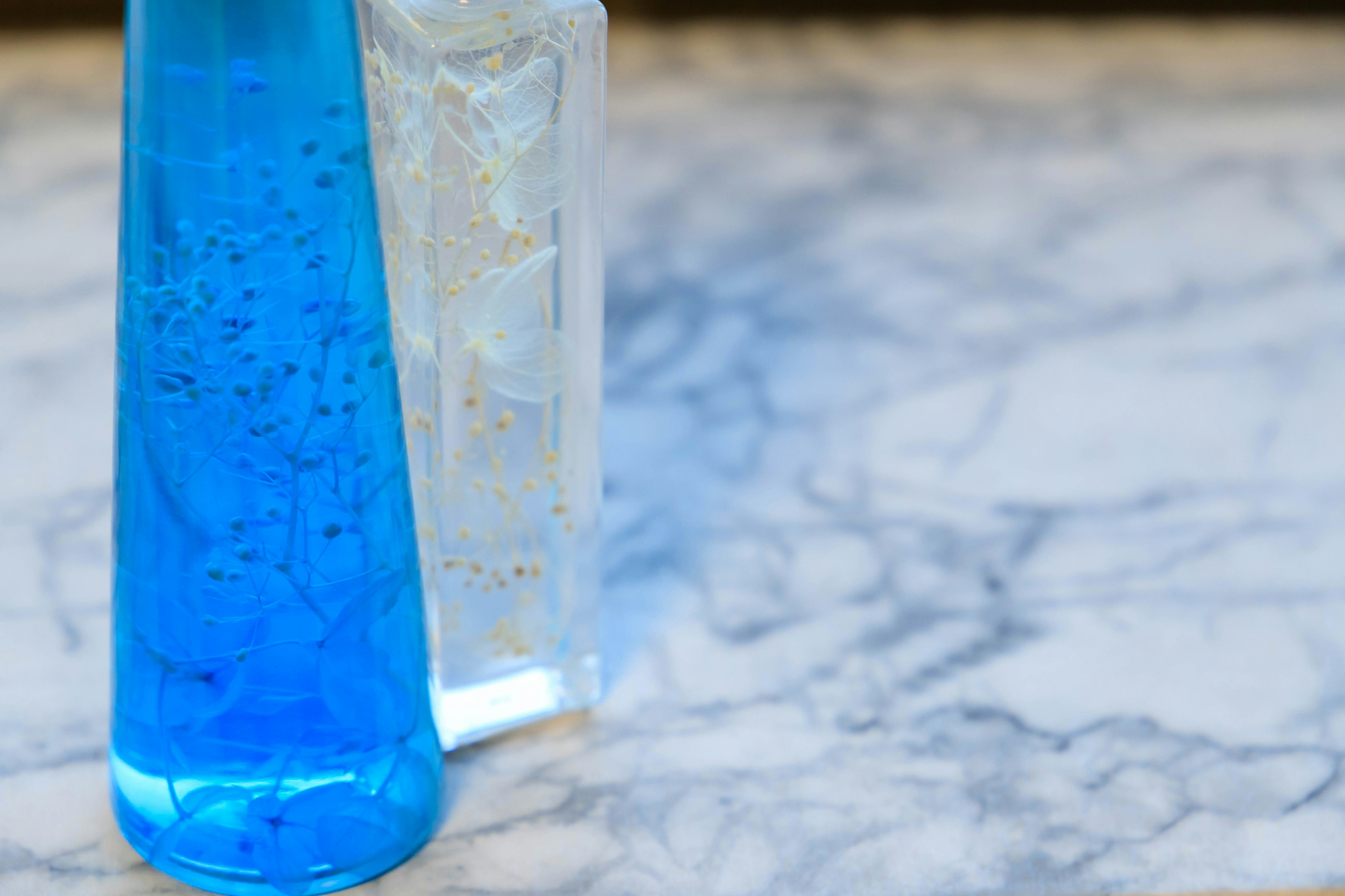 A flask with blue liquid and a block of clear ice placed on a marble surface