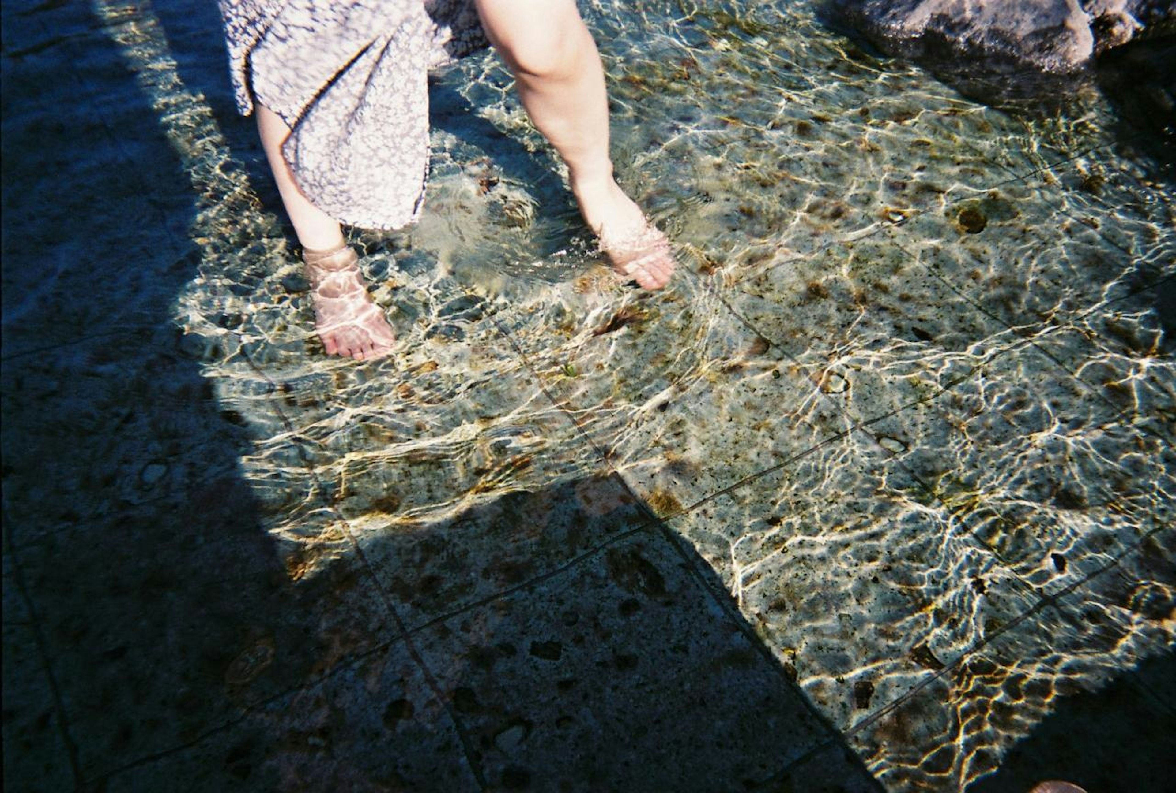 Kaki seorang wanita yang berendam di air jernih dengan pantulan