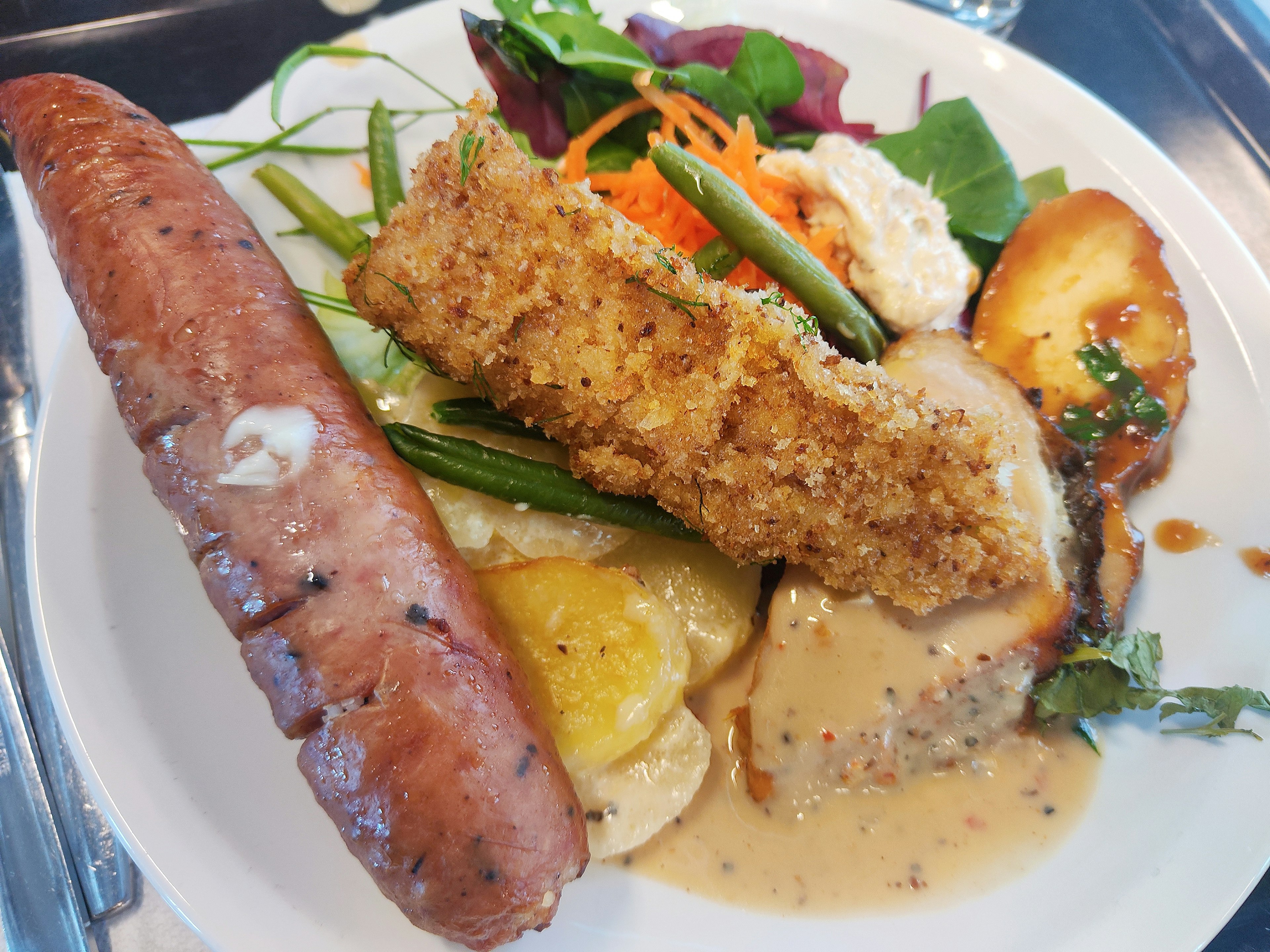 A plate featuring crispy breaded chicken and sausage accompanied by fresh vegetables and gravy