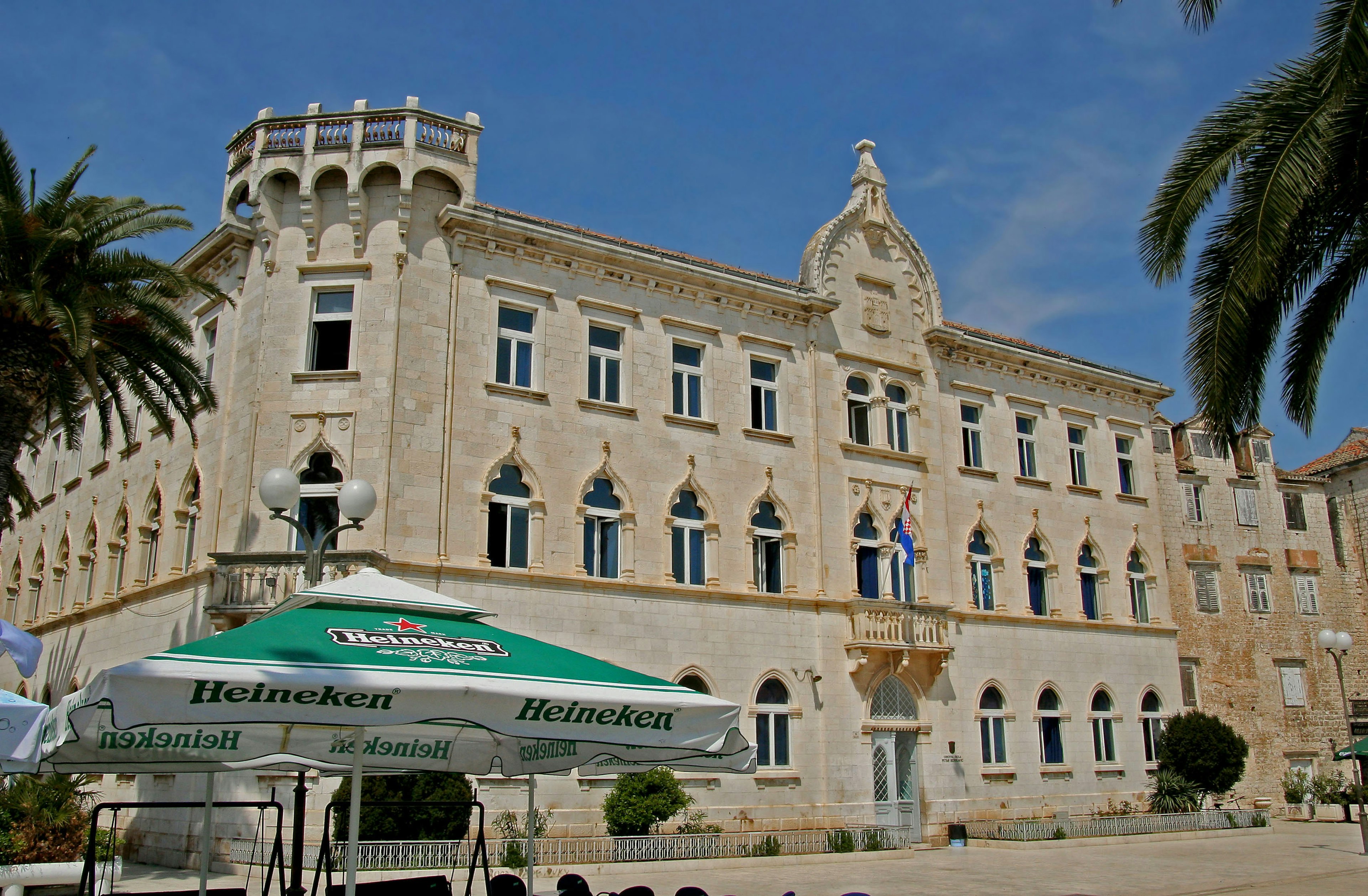 Historic building with classical architecture featuring palm trees and terrace seating