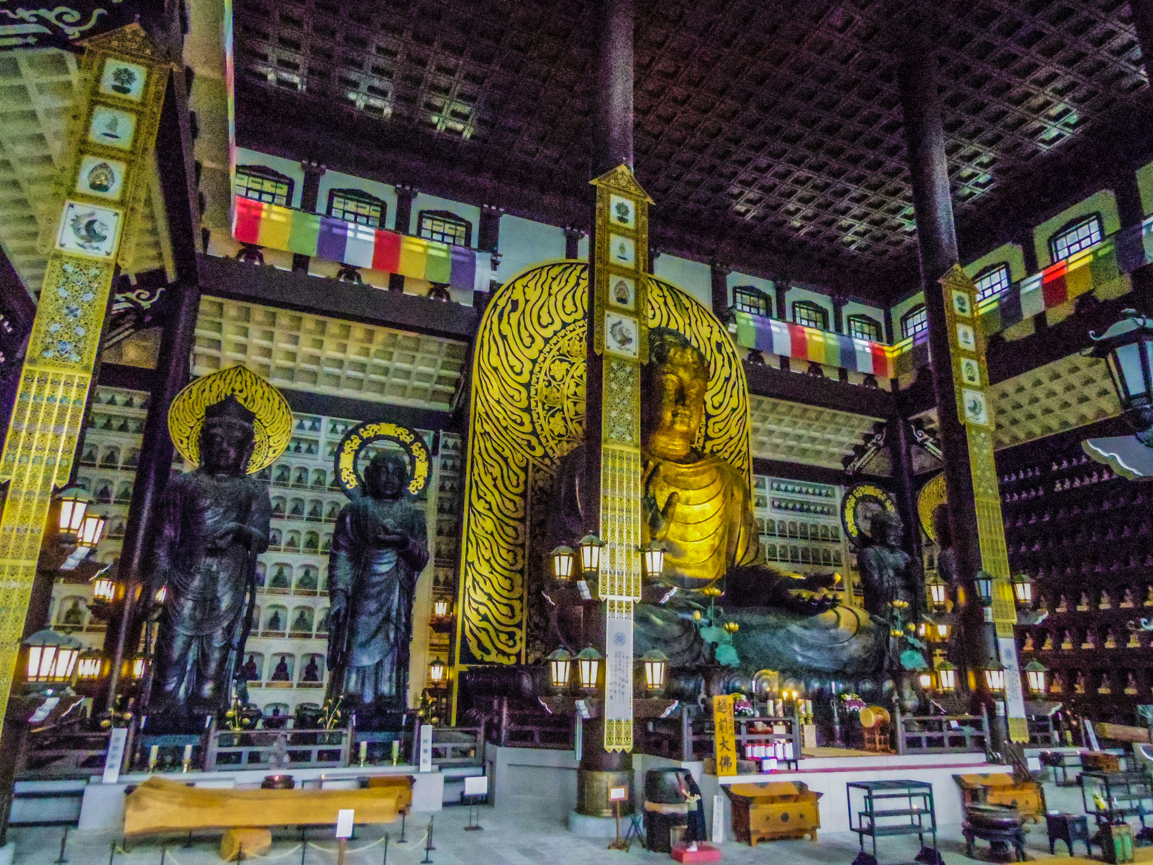 Innenraum eines Tempels mit einer großen goldenen Buddha-Statue und umliegenden schwarzen Statuen