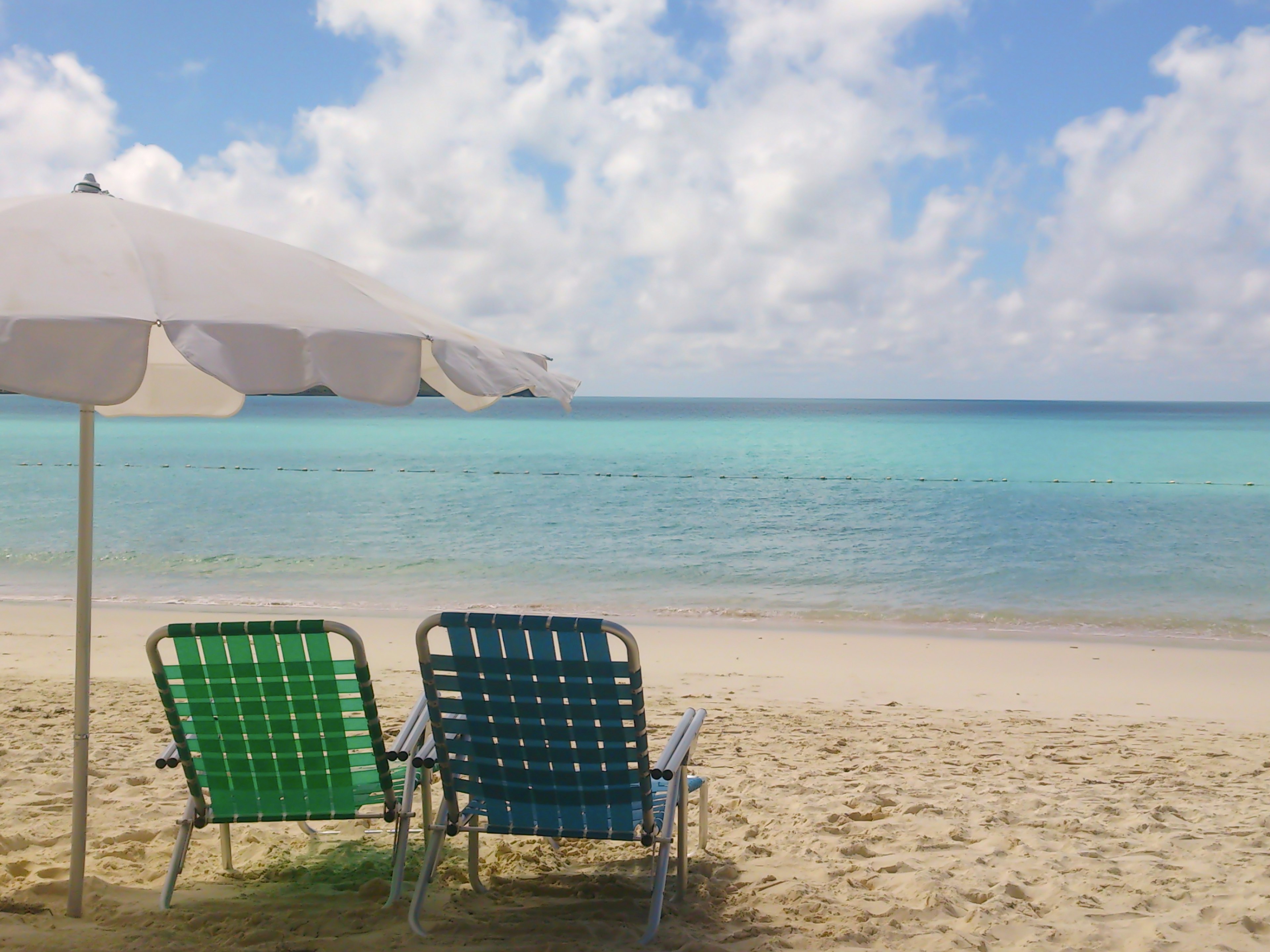 Chaises de plage vertes et bleues sur une plage de sable avec de l'eau turquoise