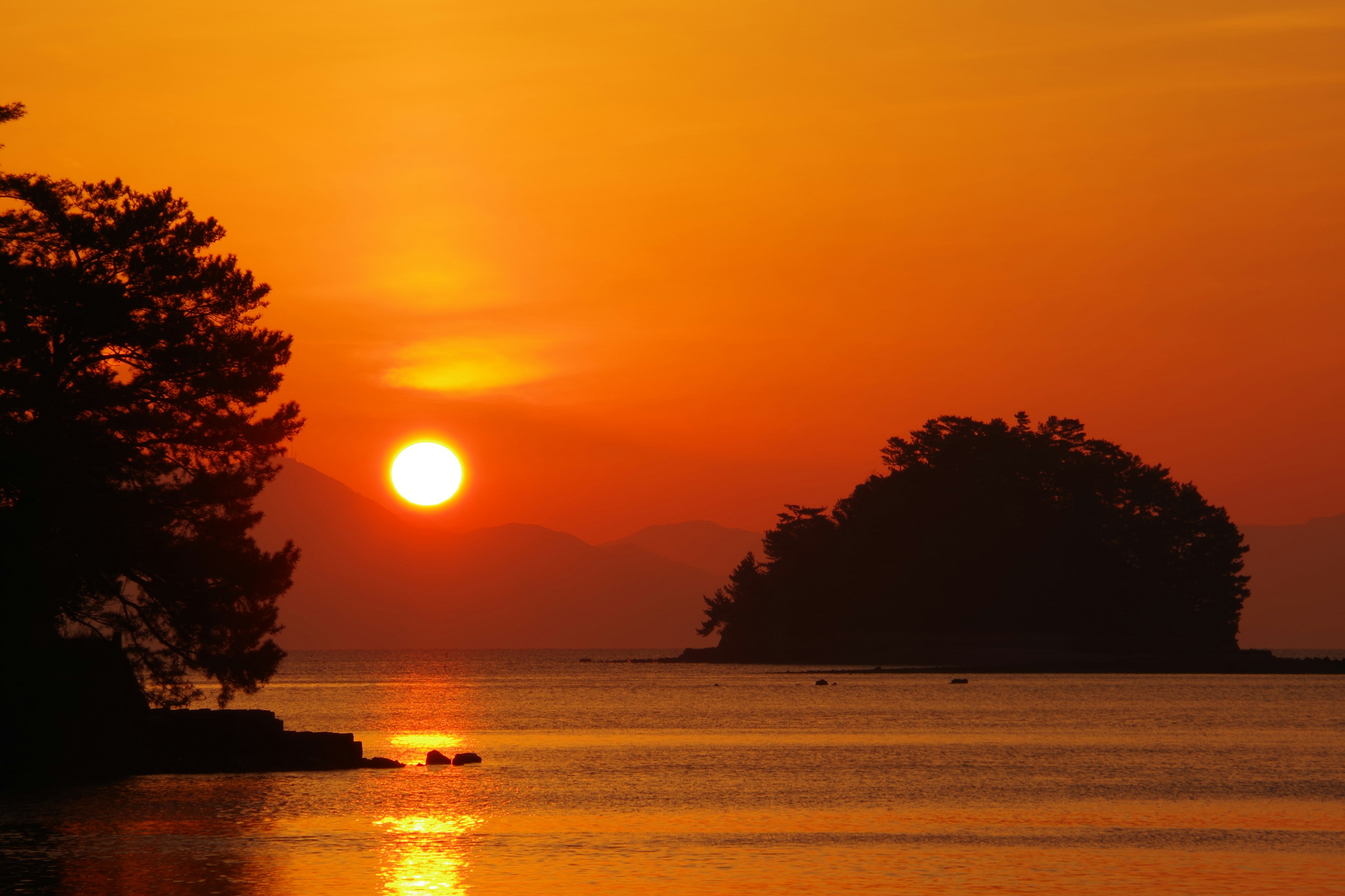 Landschaft mit Sonnenuntergang über dem Meer und Silhouette einer Insel und Bäume