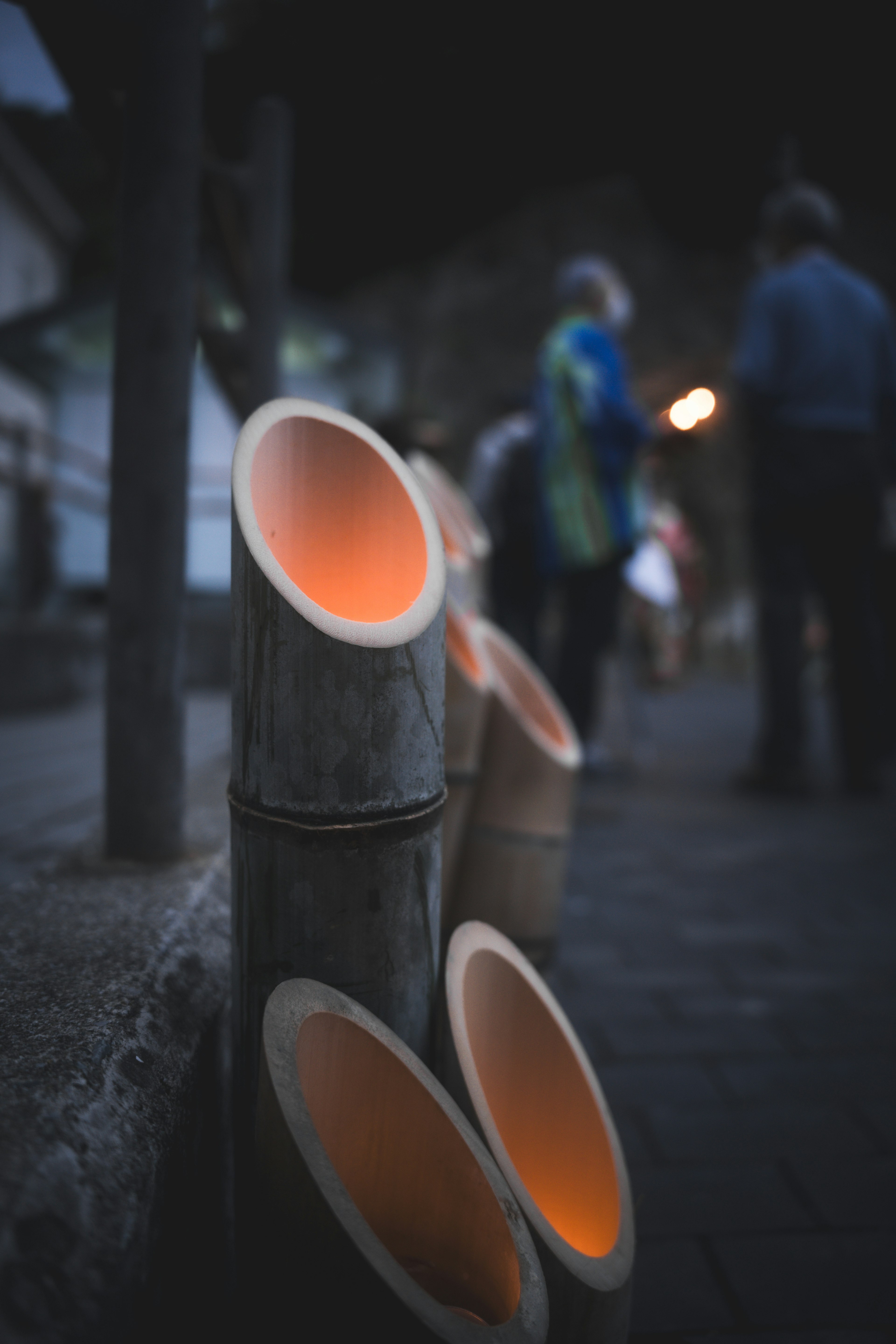 Bamboo tubes glowing softly on a night pathway with blurred figures in the background