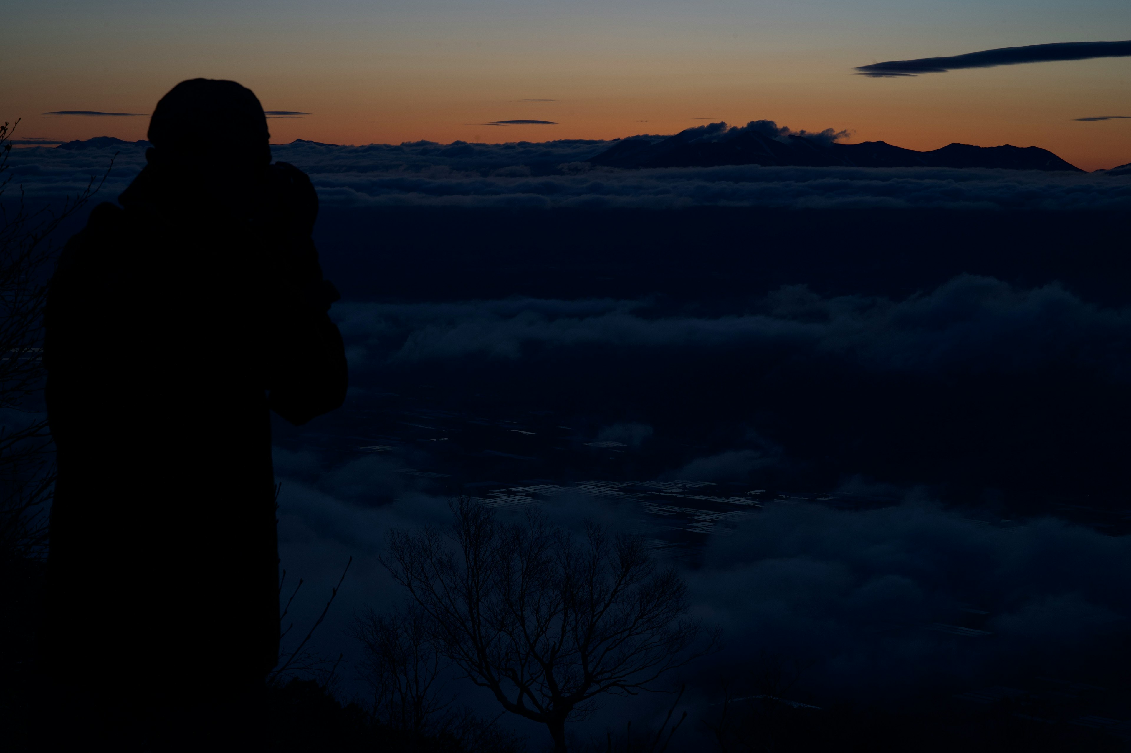 Silhouette einer Person, die auf ein Wolkenmeer bei Sonnenuntergang blickt