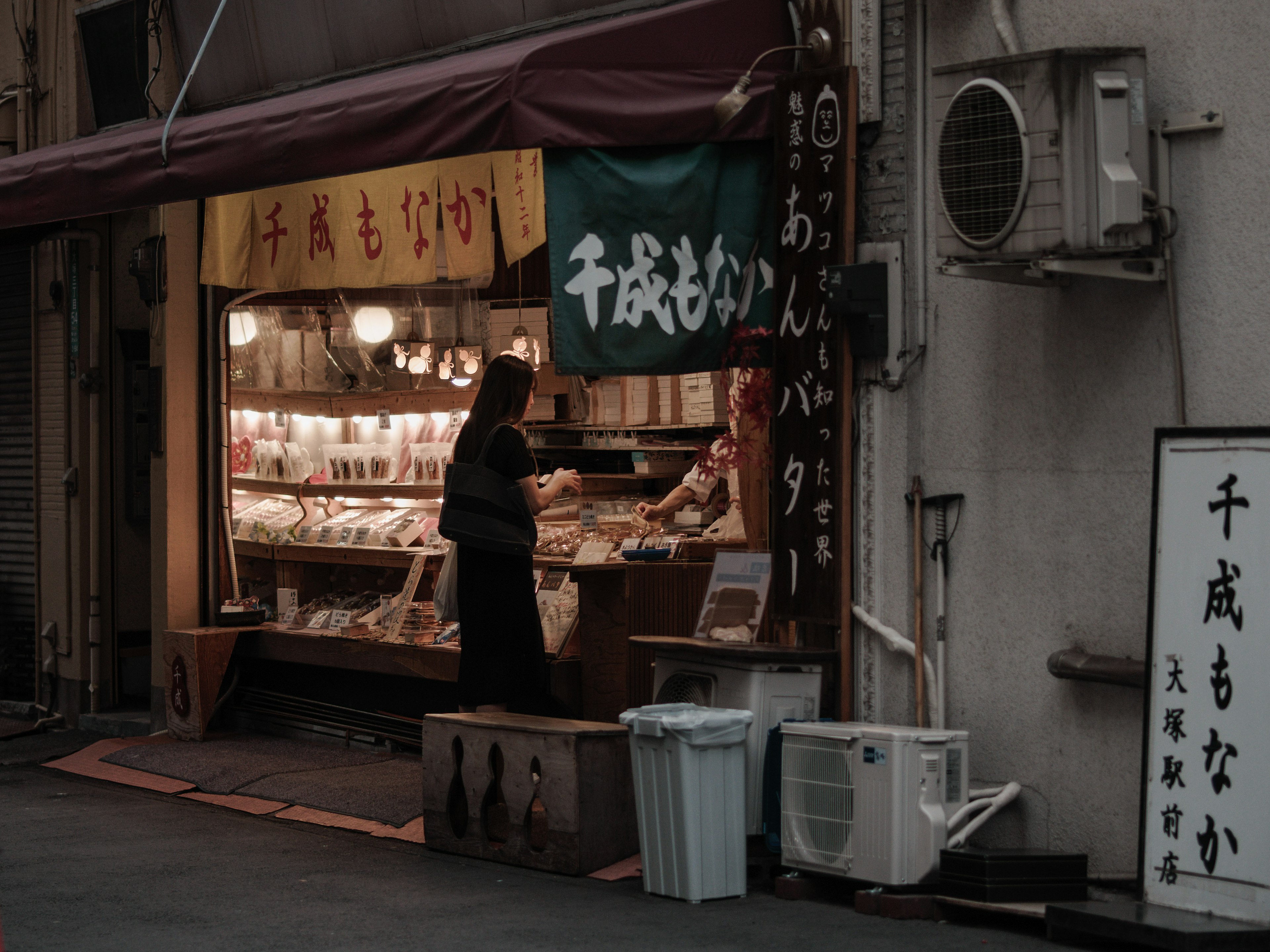 A woman selecting products in a small shop on a dimly lit street