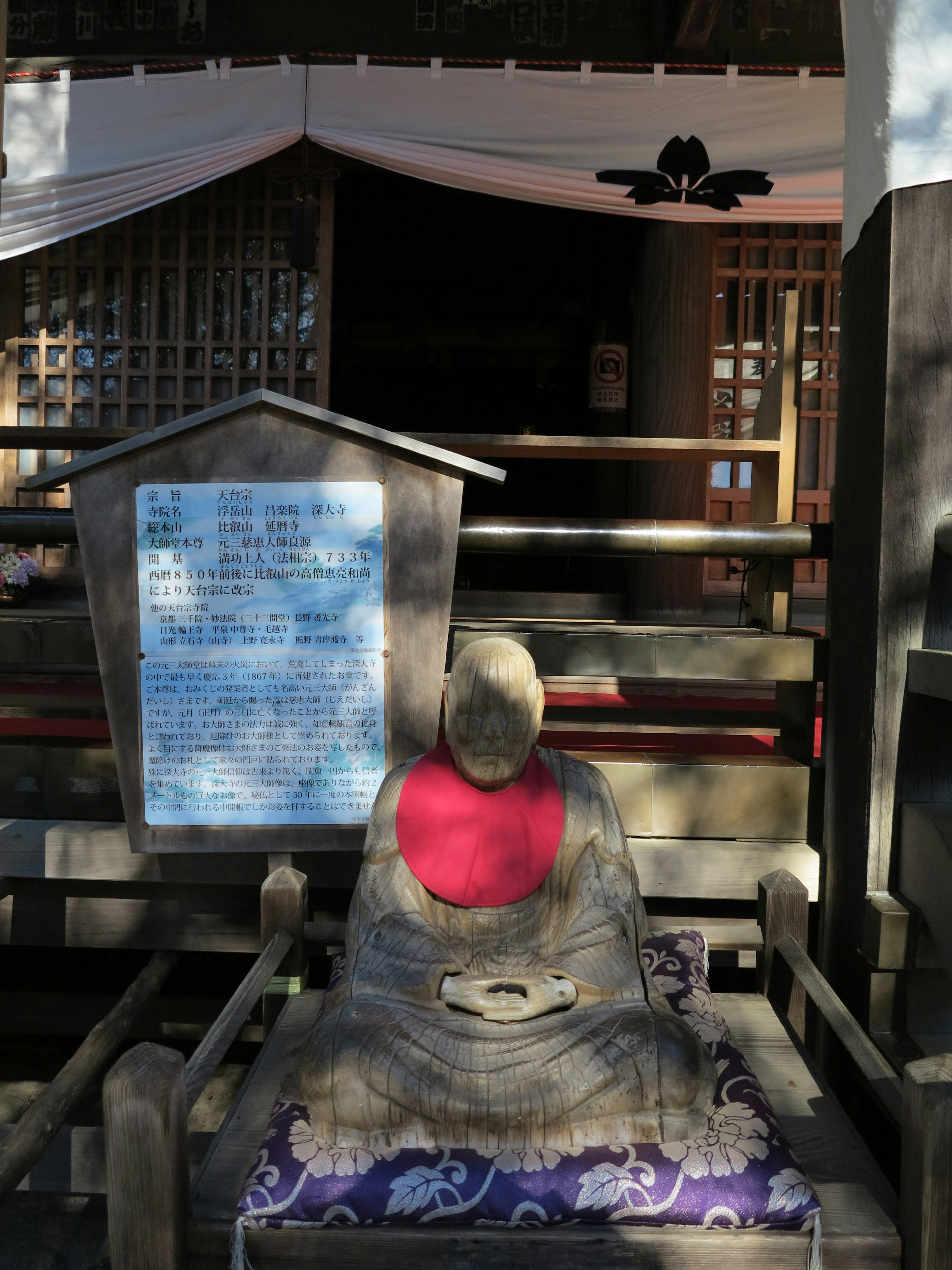 Seated Buddha statue wearing a red cloth with a building in the background