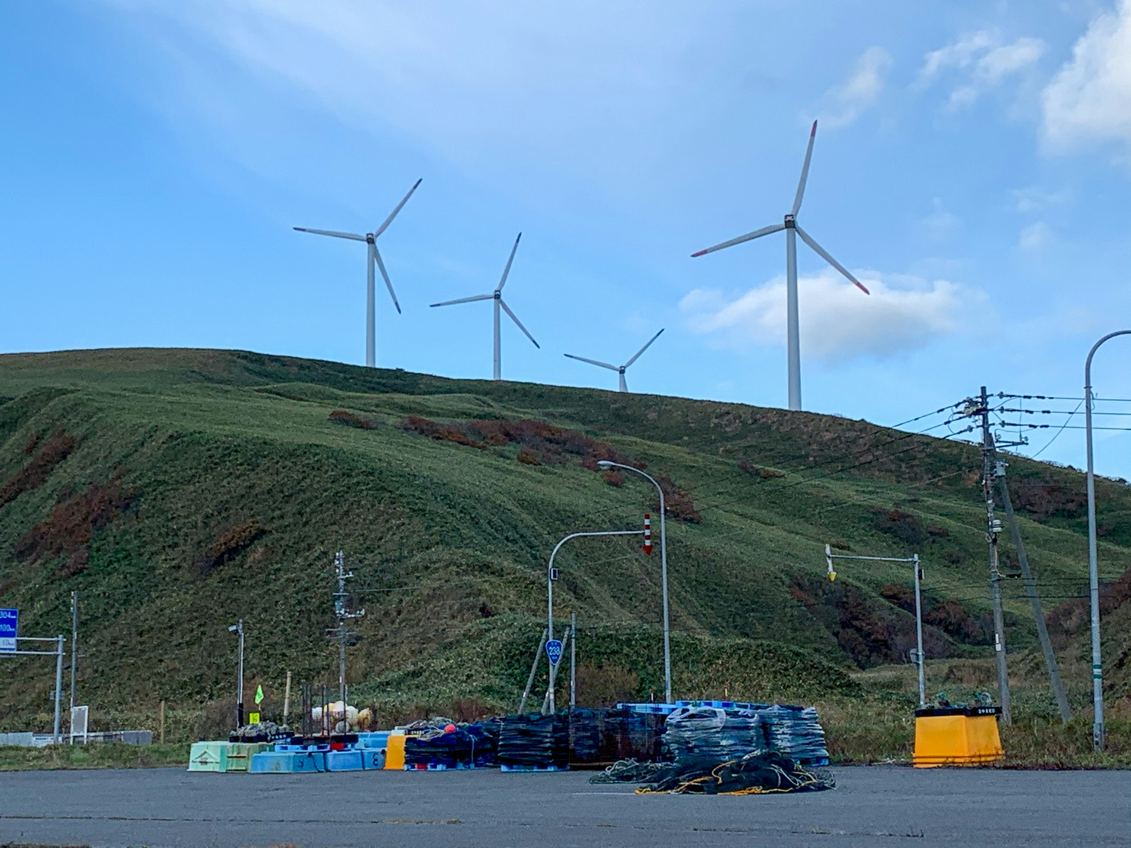 A landscape featuring wind turbines on a green hill under a blue sky