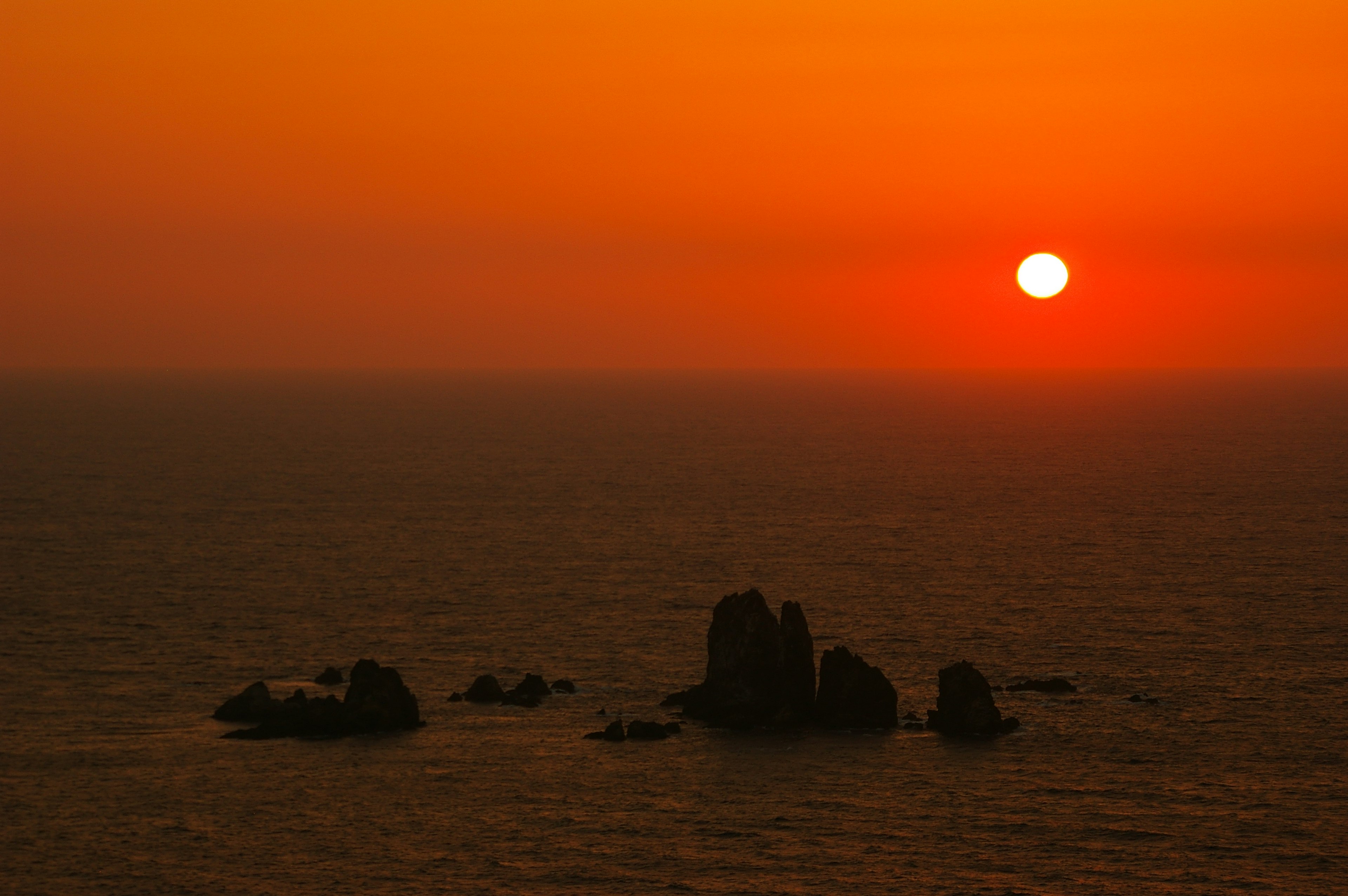 Sunset over the ocean with rocks silhouetted against an orange sky