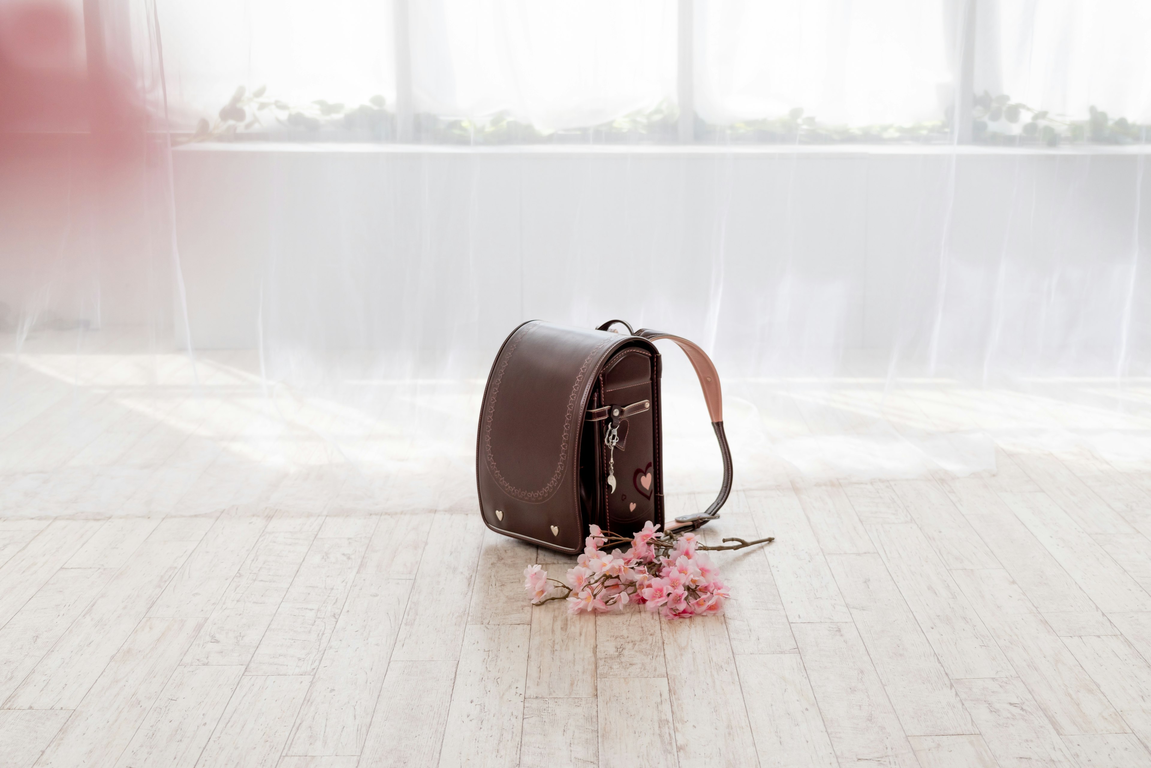 Sac à bandoulière marron avec des fleurs roses sur le sol dans un cadre lumineux