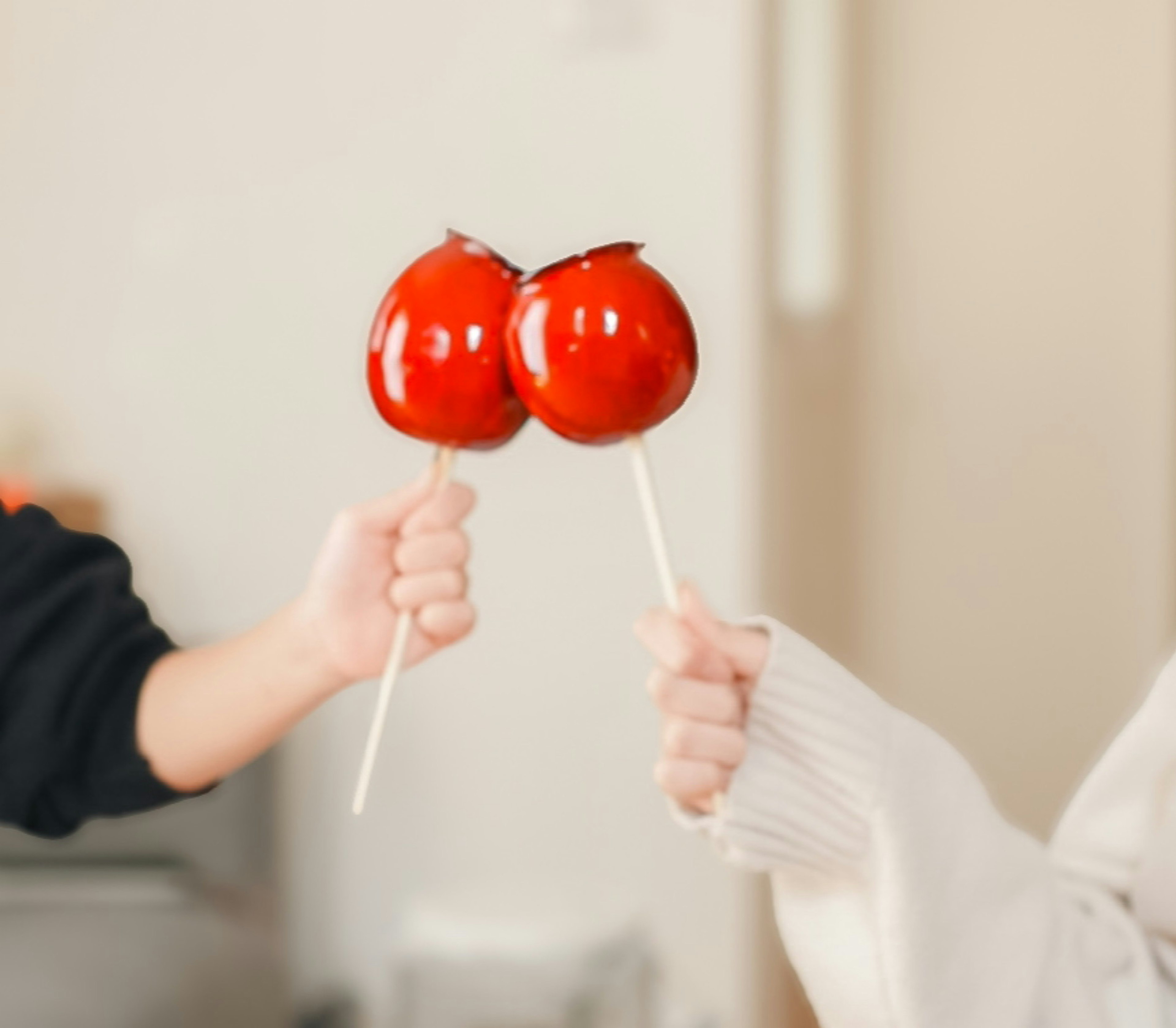 Dos manos sosteniendo manzanas de caramelo rojas brillantes enfrentadas