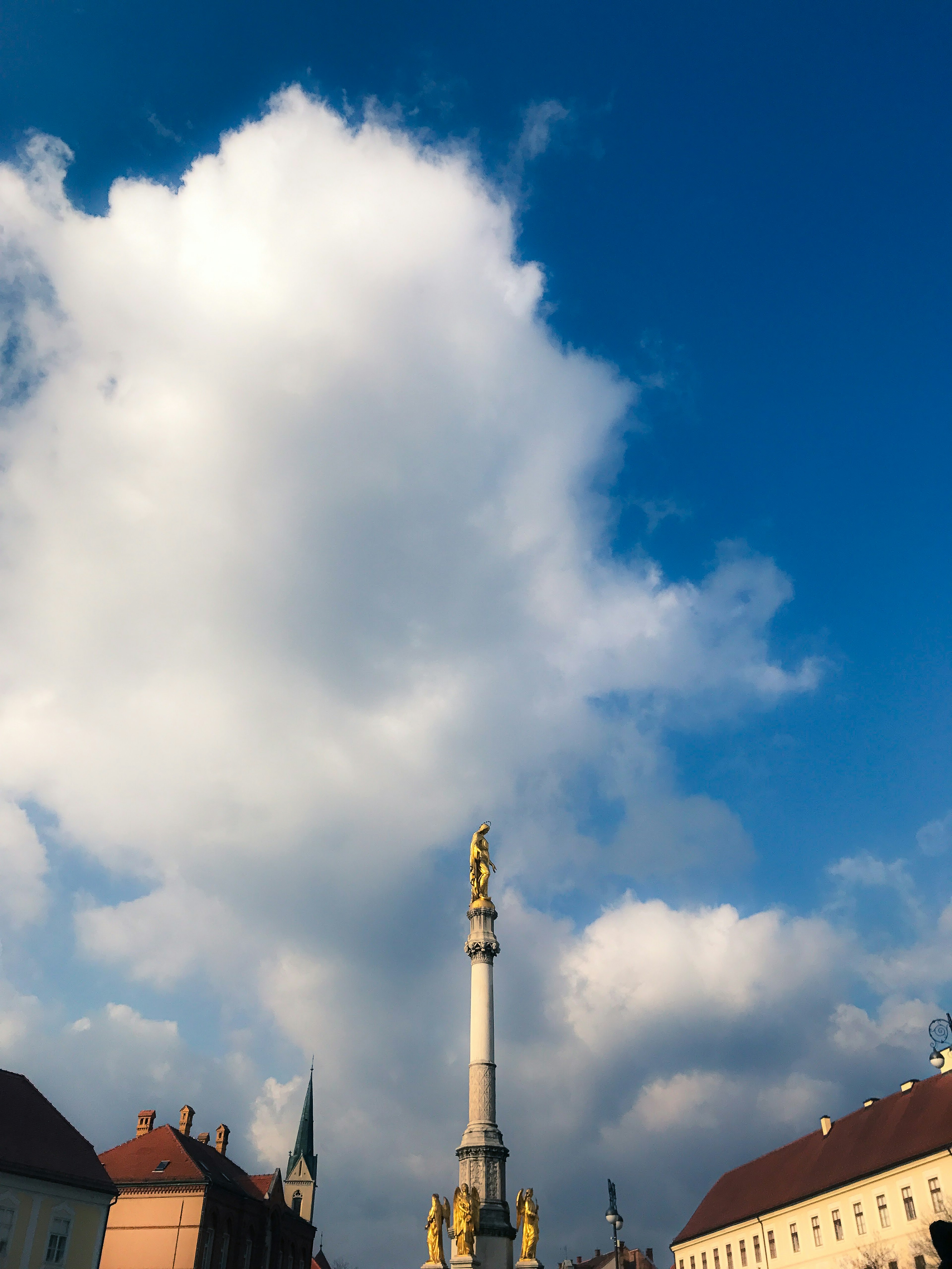 Une vue d'une place avec une colonne dorée sous un ciel bleu et des nuages blancs