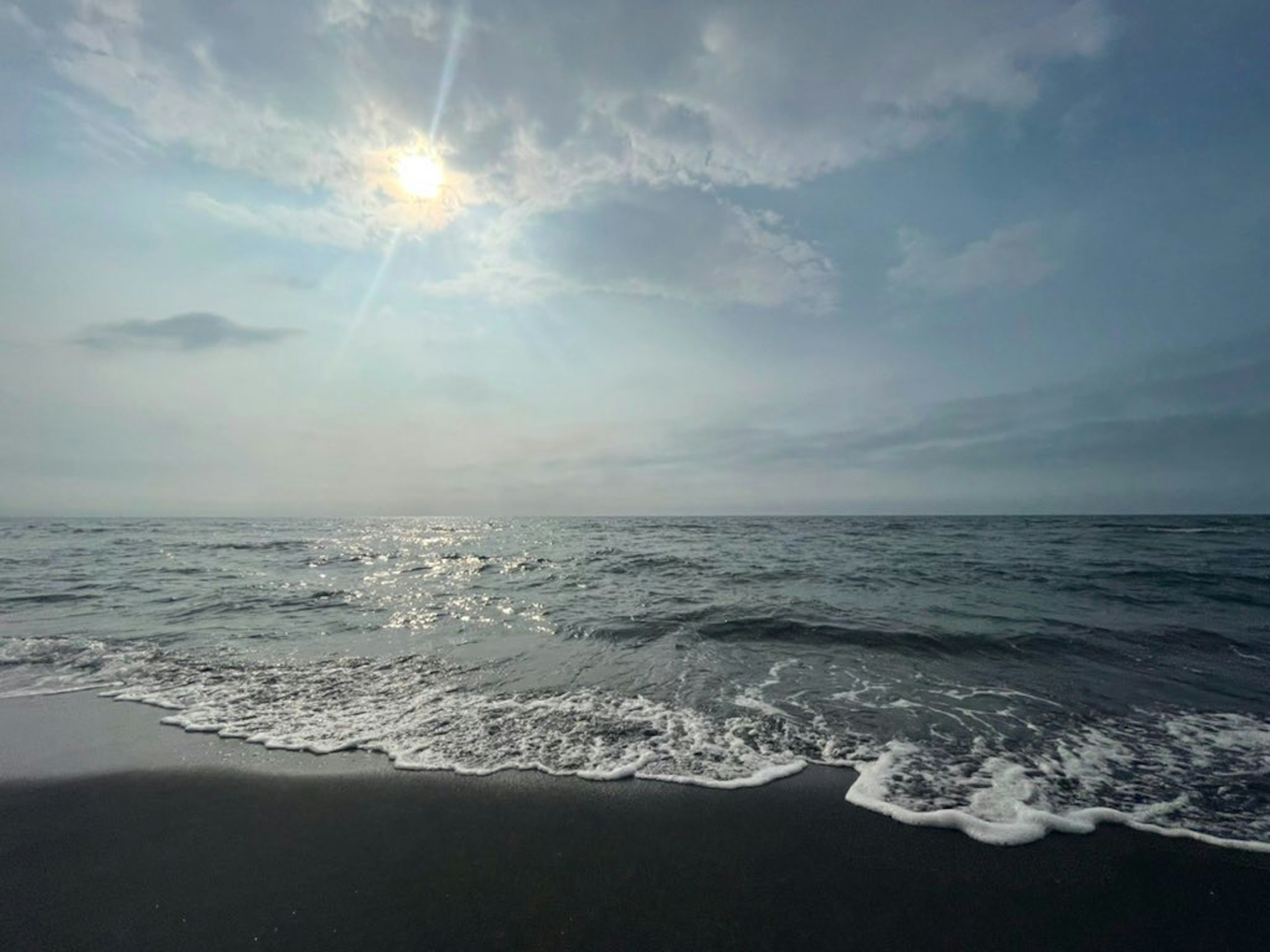 Pemandangan laut dengan ombak yang menyapu pantai dan cahaya matahari yang memantul di air