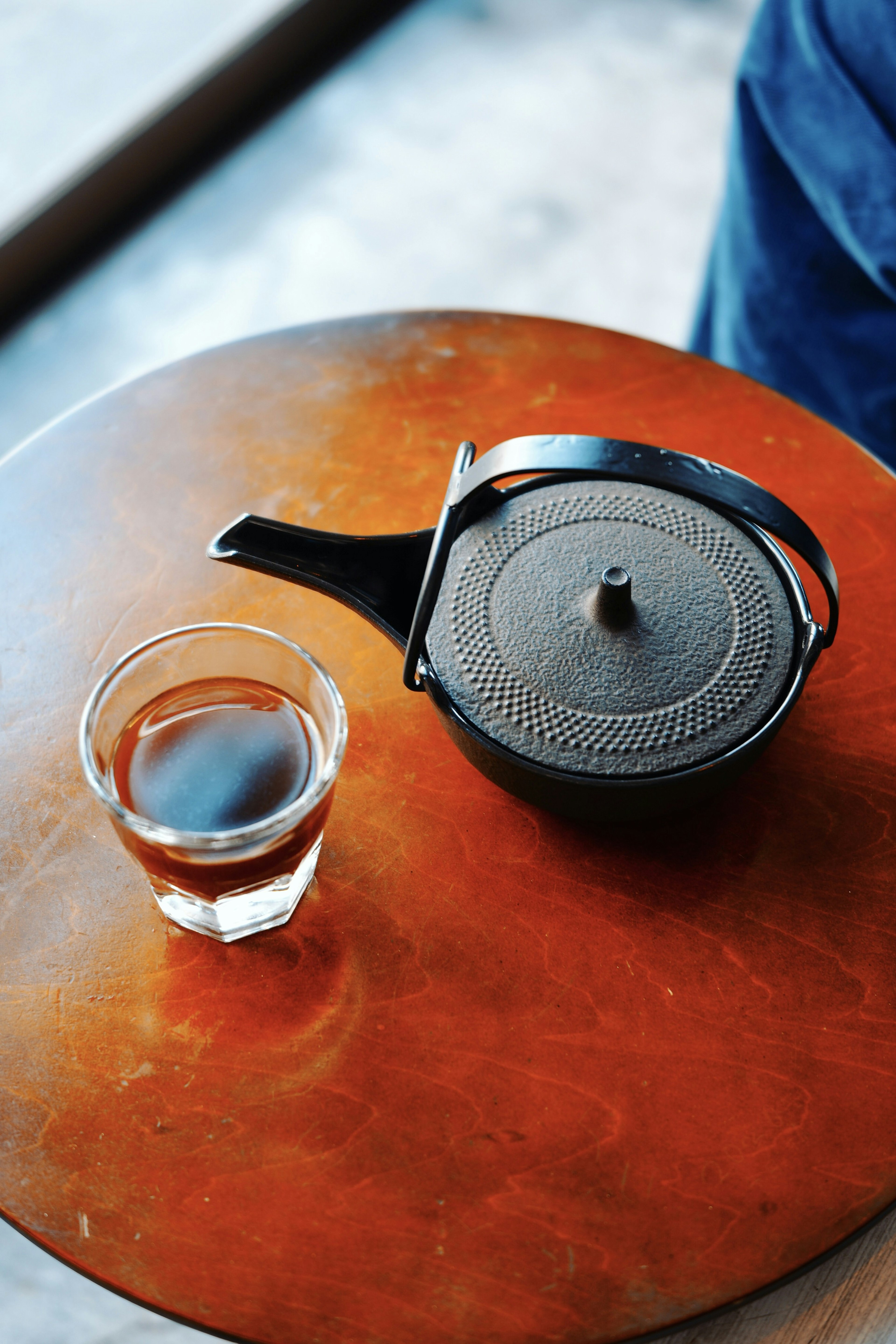 Schwarze Teekanne und transparentes Glas mit Tee auf einem Holztisch