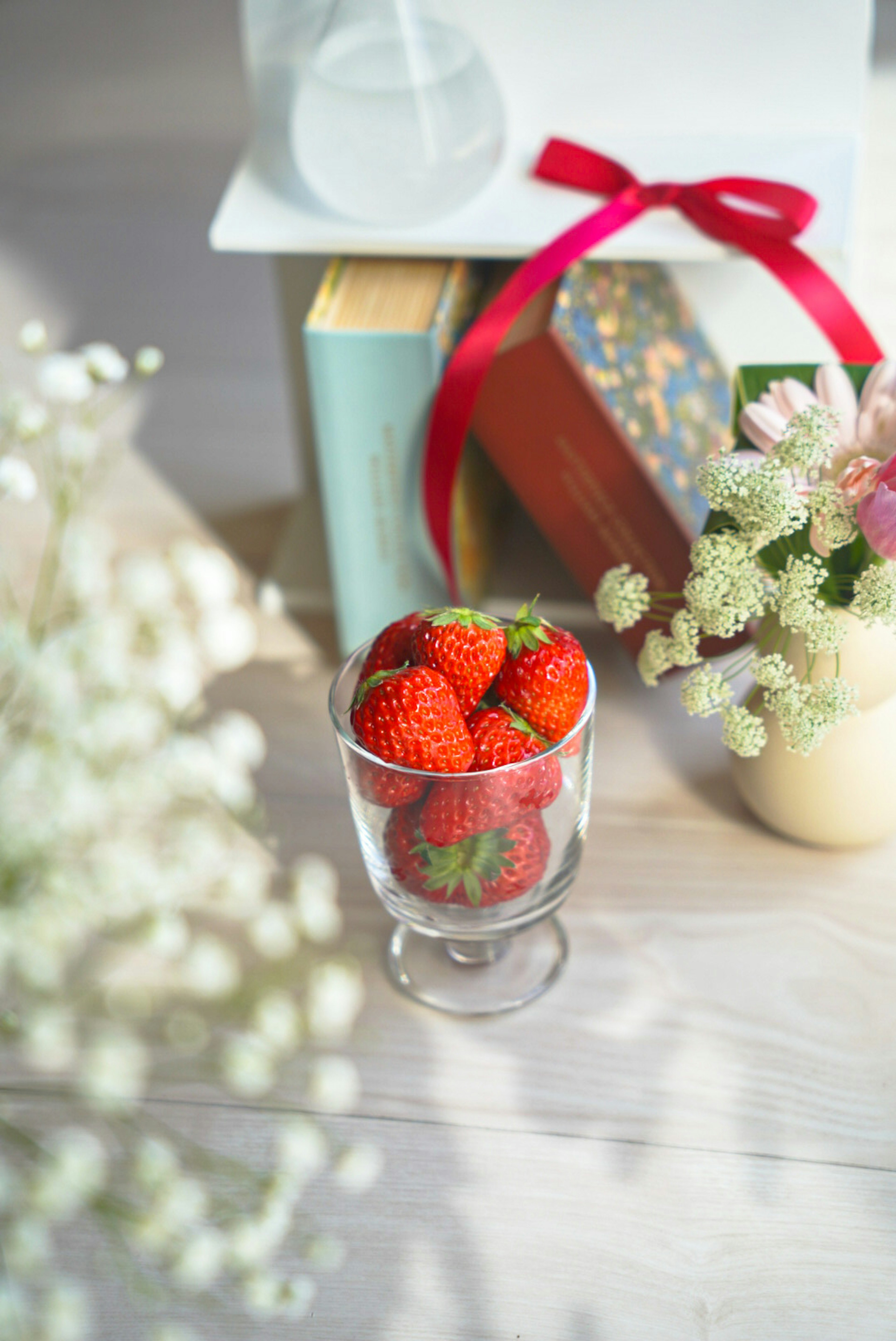 Frische Erdbeeren in einem Glas mit Büchern und Blumen auf einem Tisch