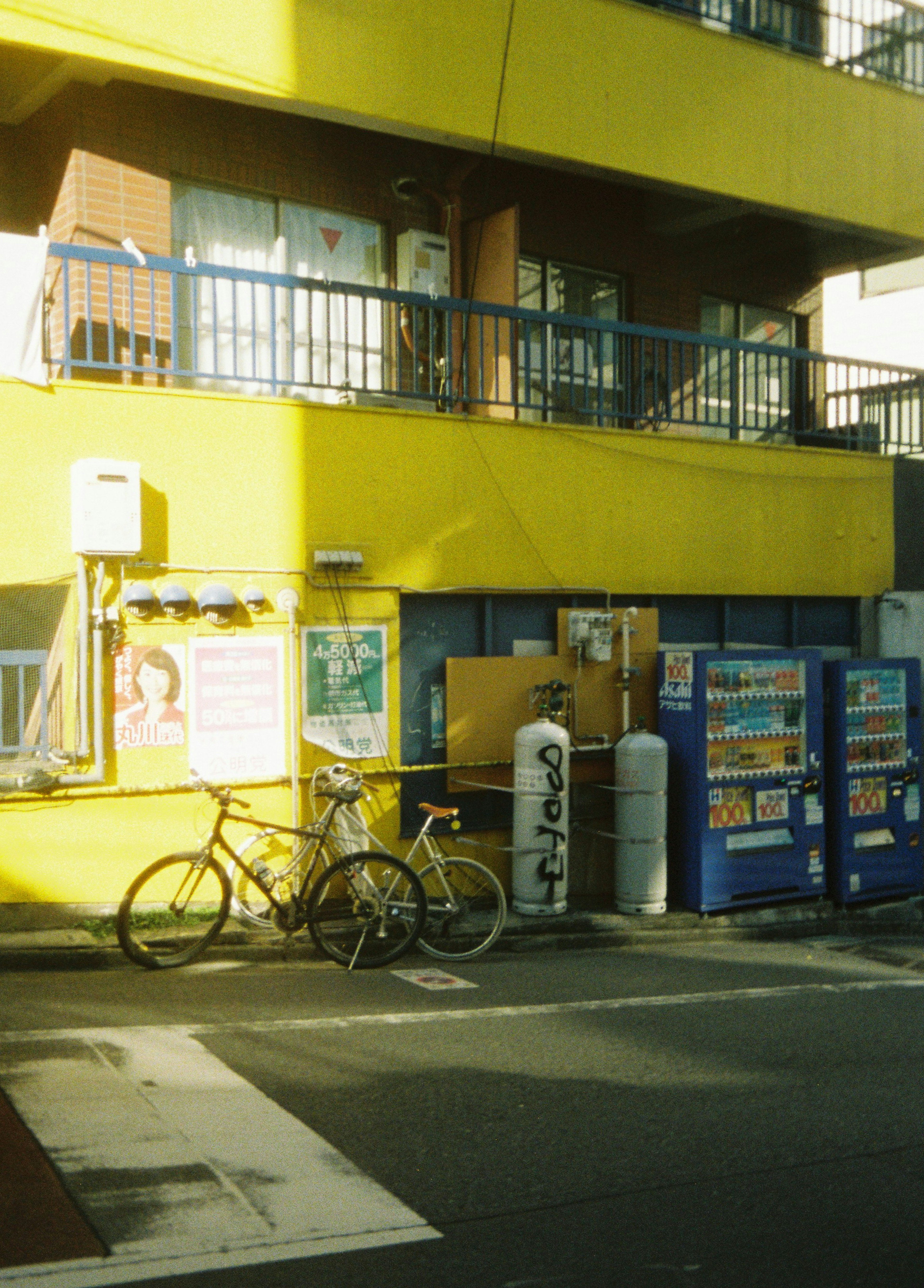 Scene with bicycles and vending machines outside a yellow building