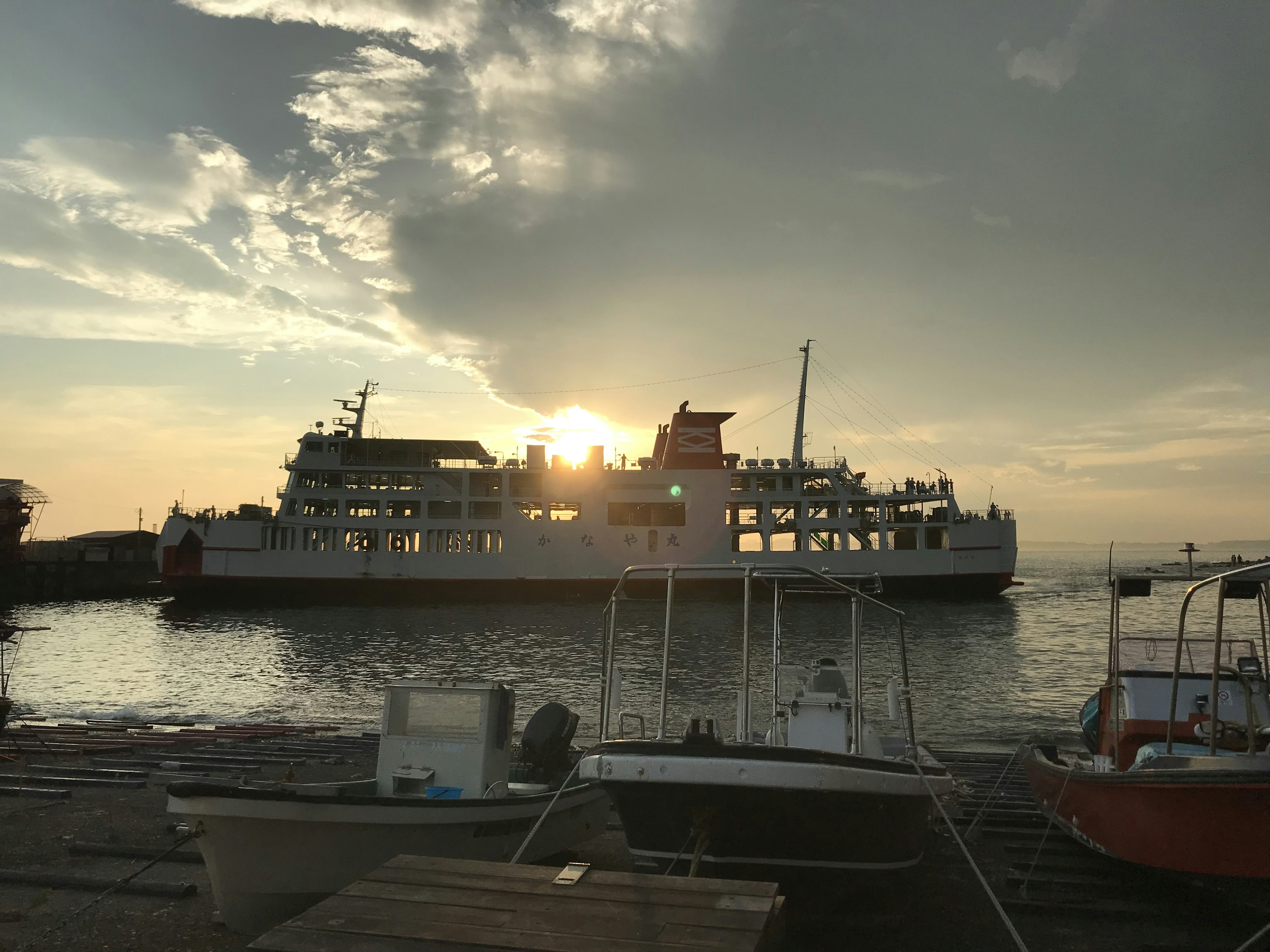 Ferry in controluce al tramonto con piccole barche in primo piano