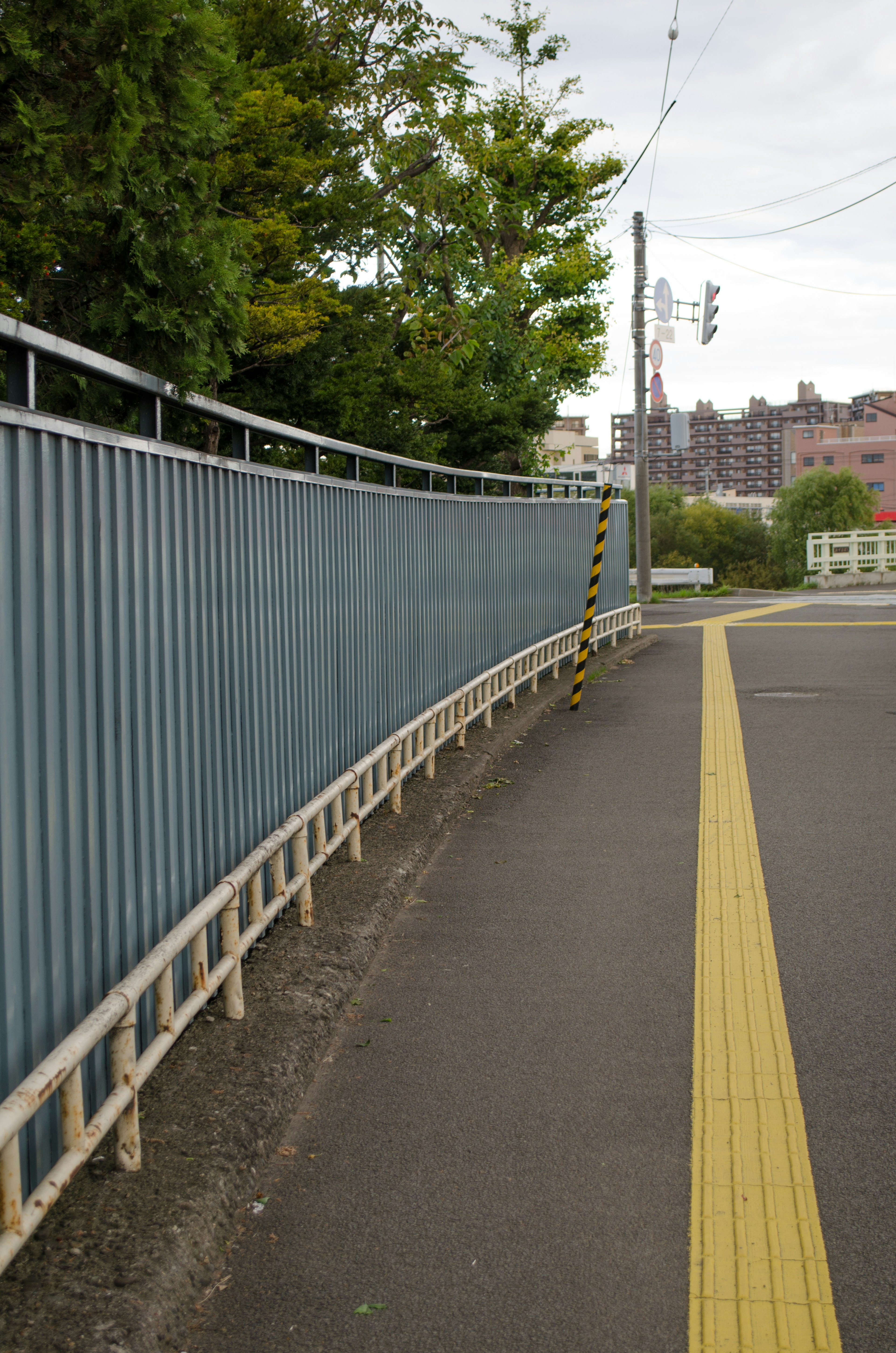 Curved blue metal fence along a road with yellow line