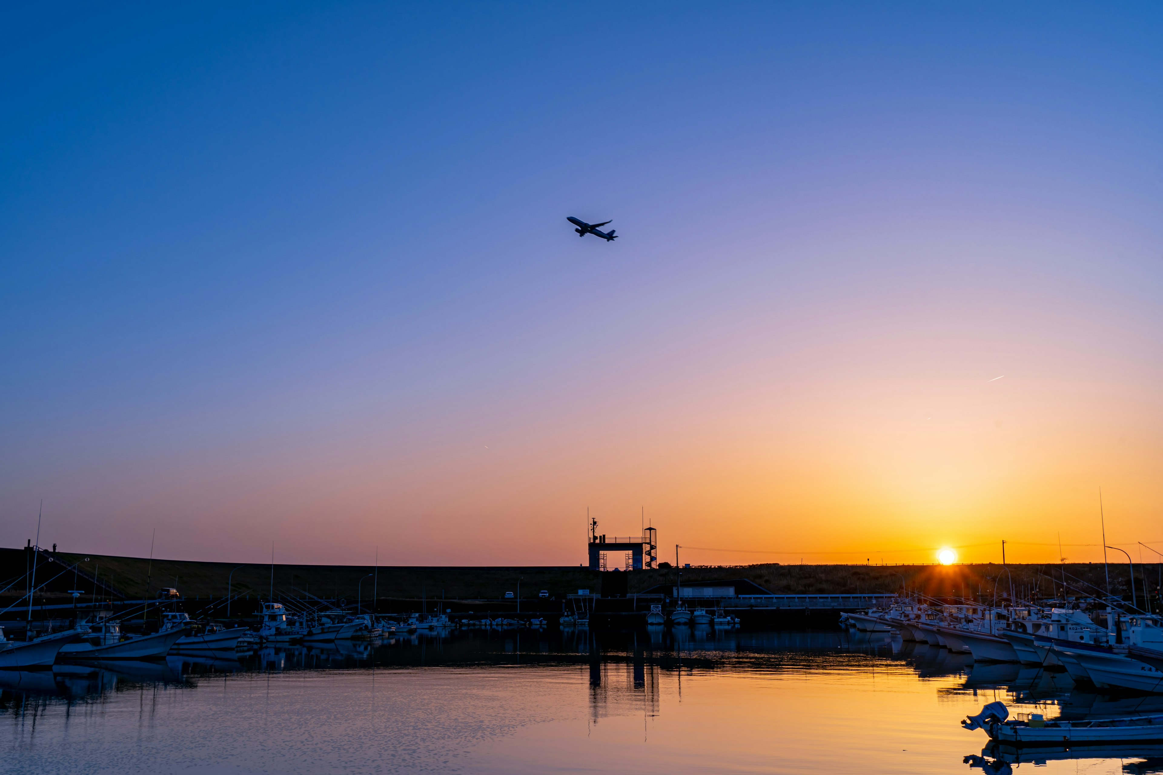 Un avion survolant un port au coucher de soleil avec des reflets dans l'eau calme