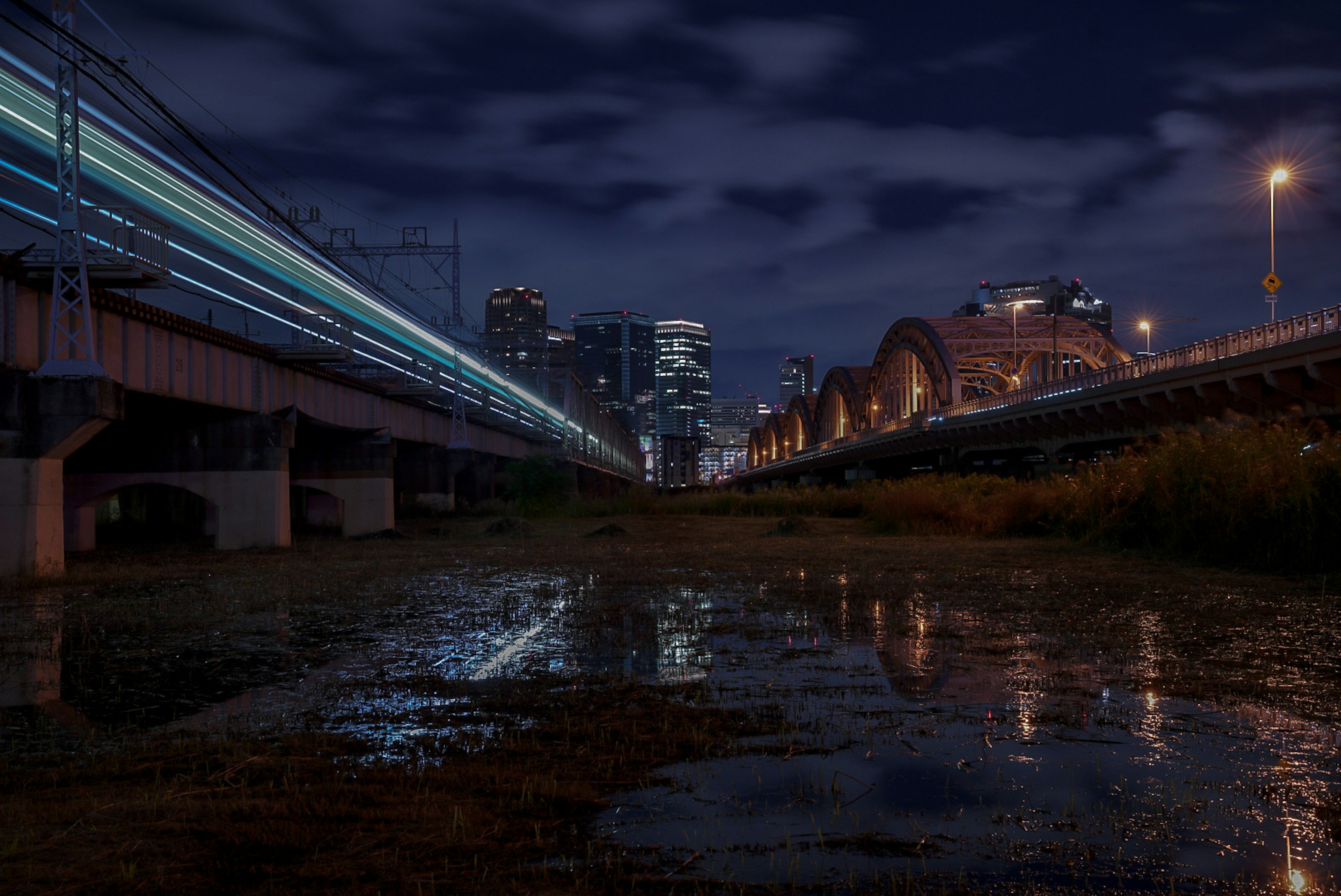 ทิวทัศน์เมืองในเวลากลางคืนที่มีรางรถไฟและการสะท้อนในแอ่งน้ำ