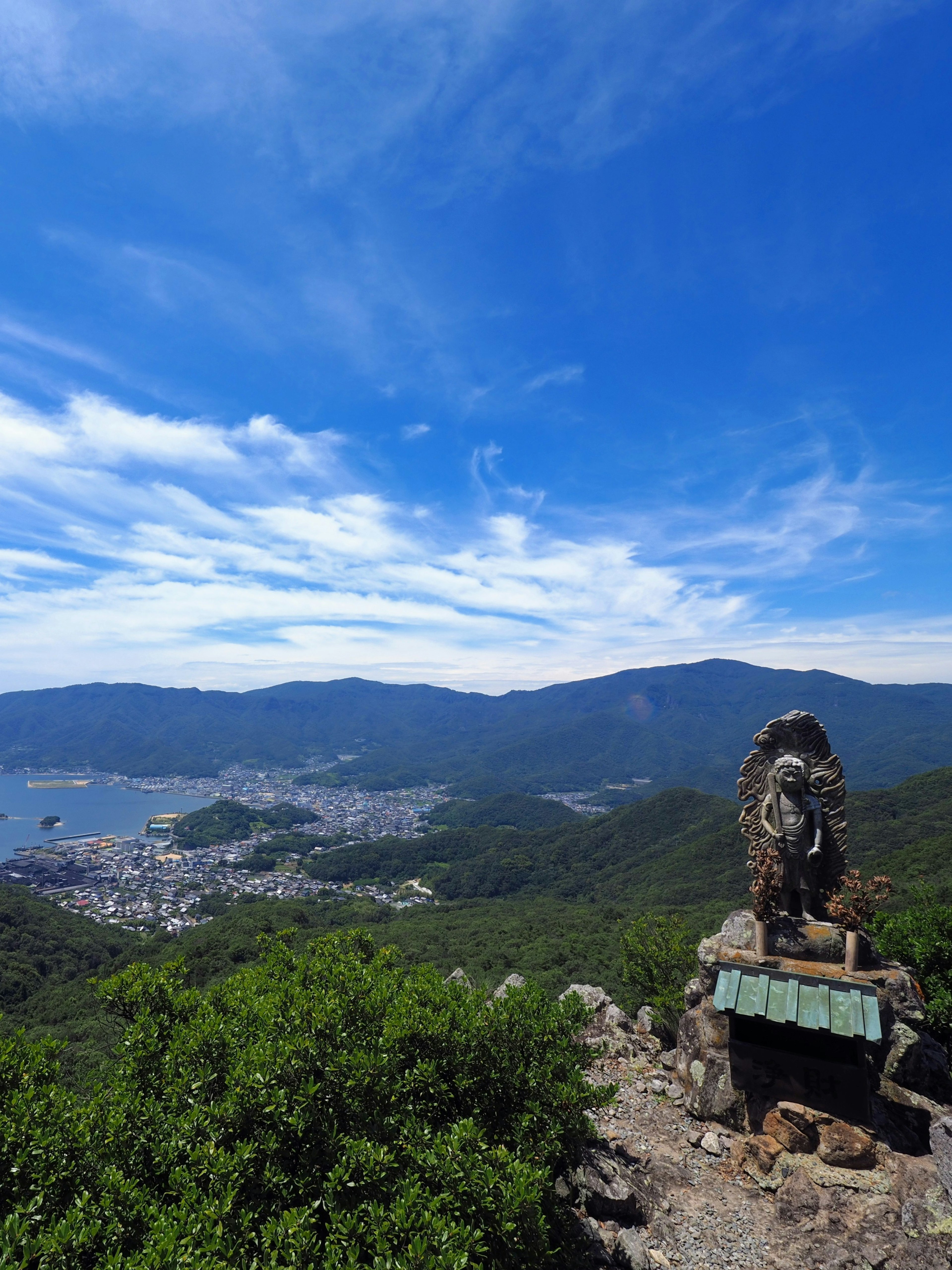 Vista panorámica de montañas y ciudad bajo un cielo azul con escultura de roca