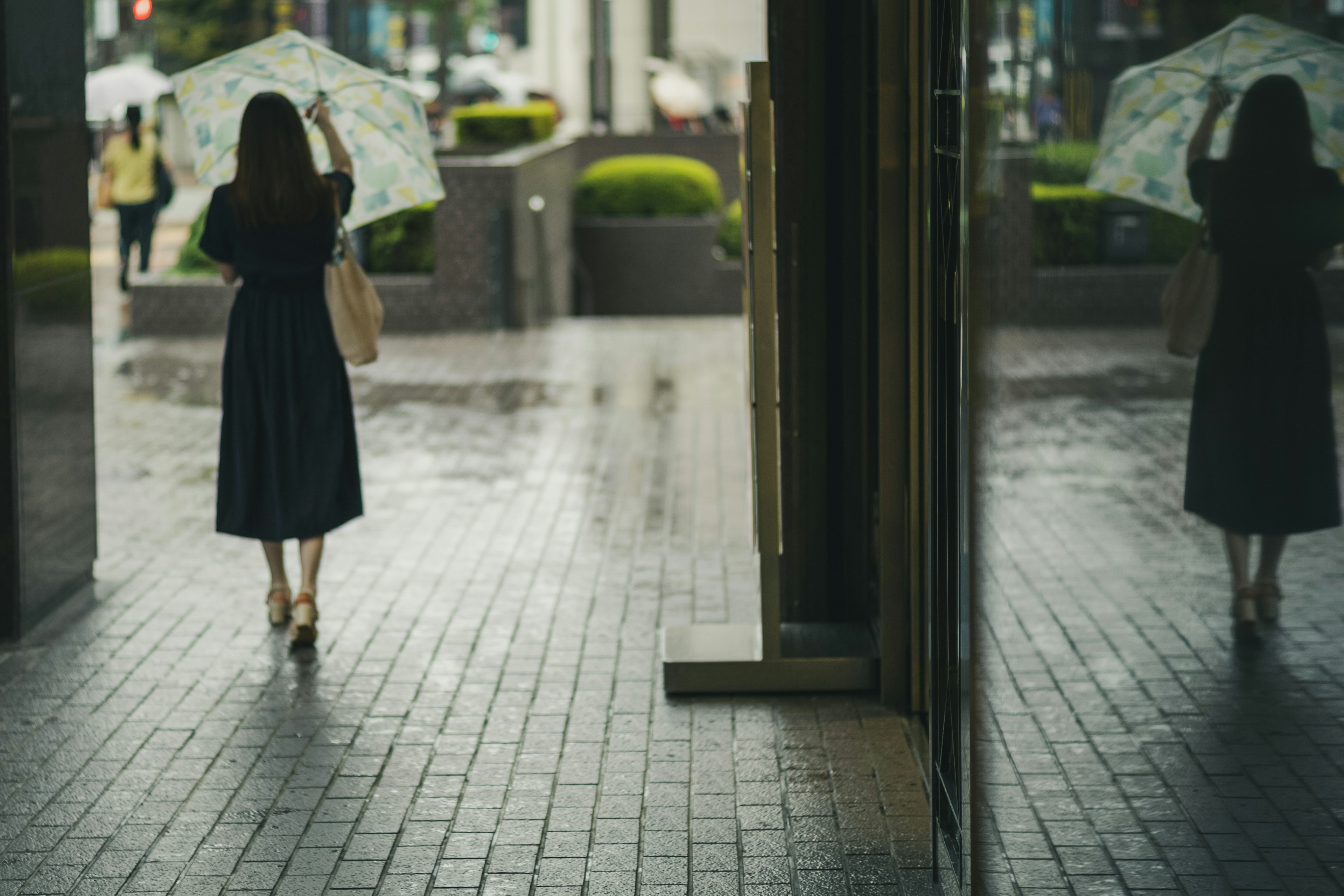 Una mujer caminando con un paraguas bajo la lluvia reflejada en un paisaje urbano