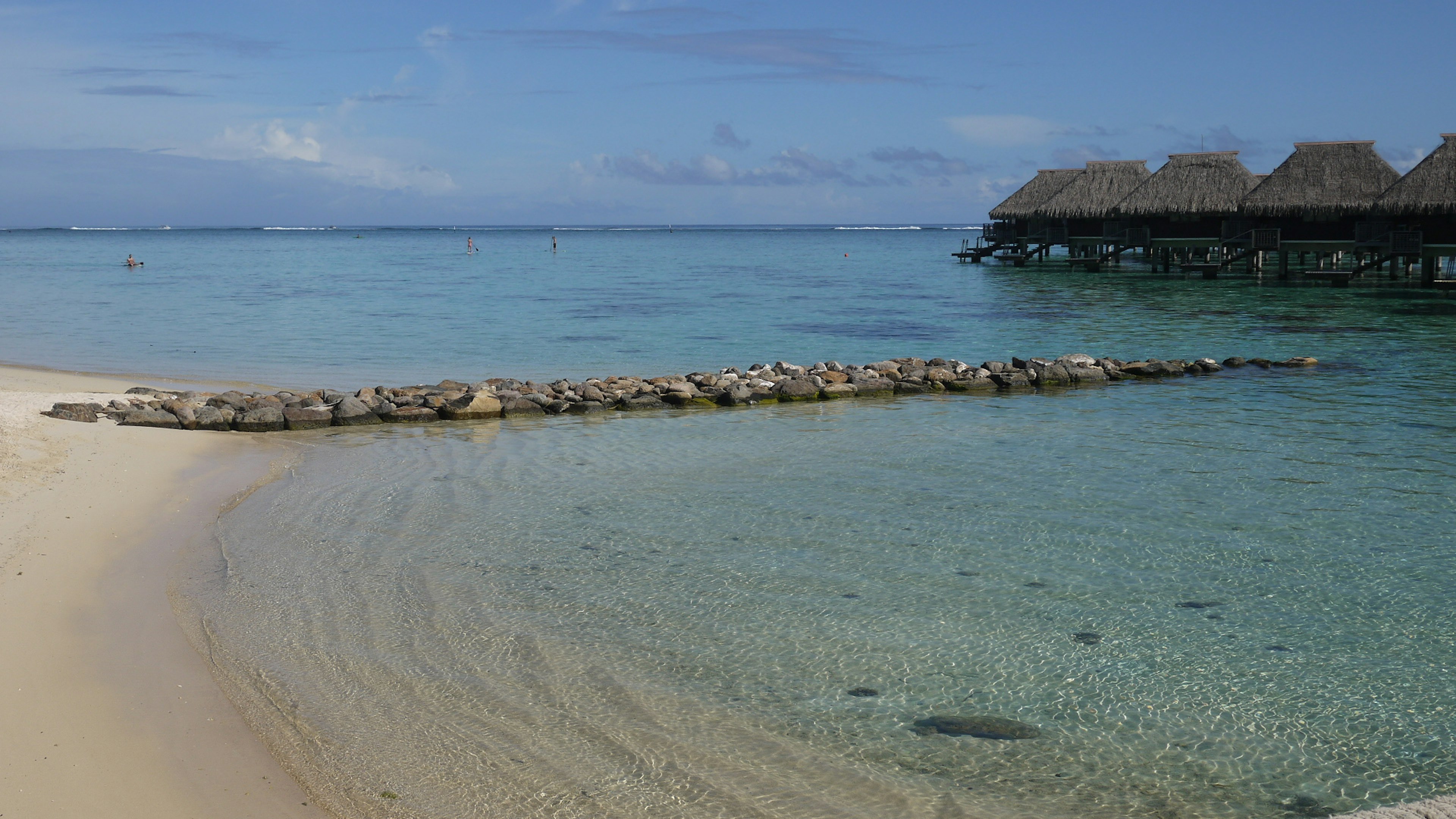 Malerscher Blick auf den blauen Ozean und den ruhigen Sandstrand mit einem Steindeich und Hütten