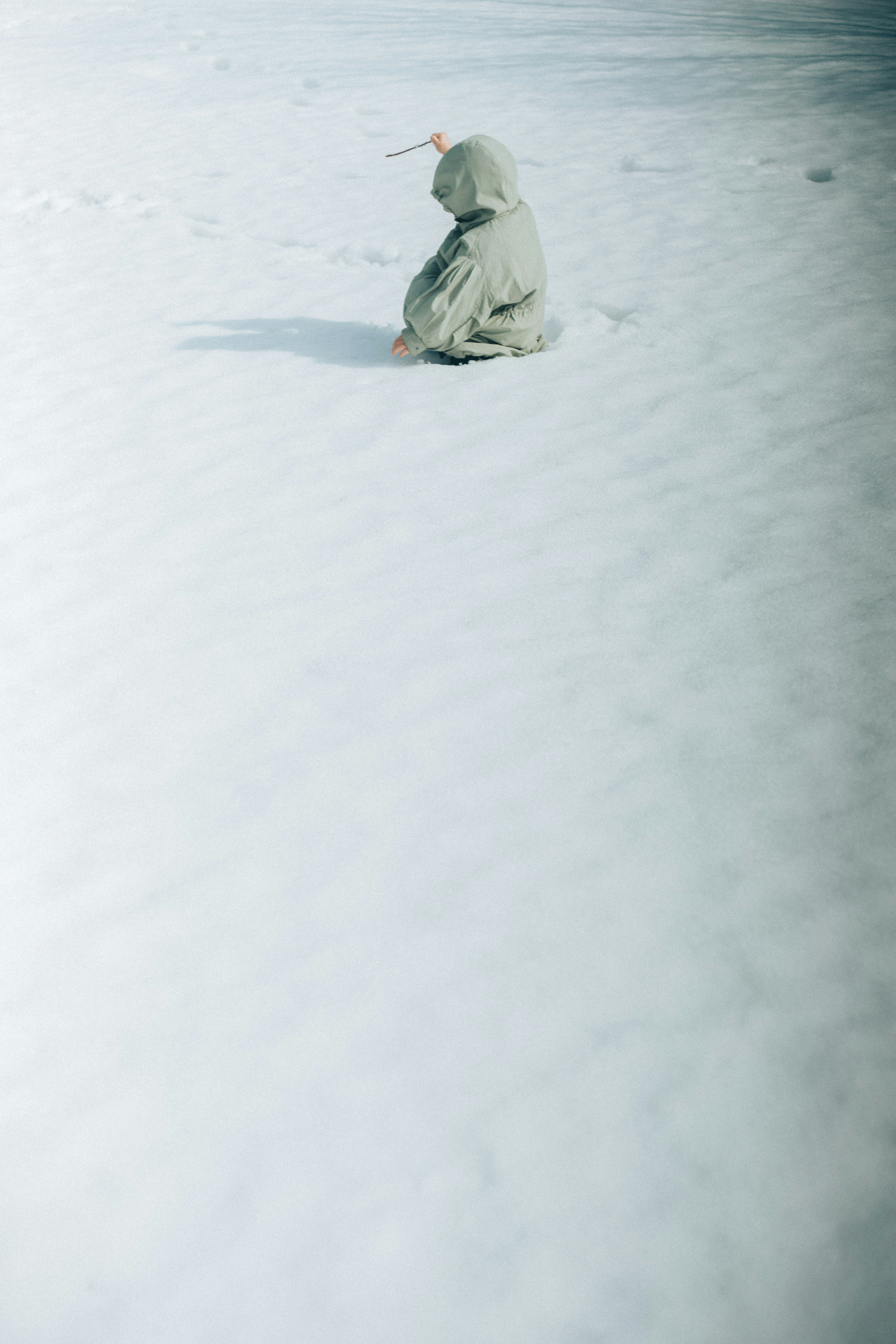 Kind sitzt im Schnee mit einem hellgrünen Mantel