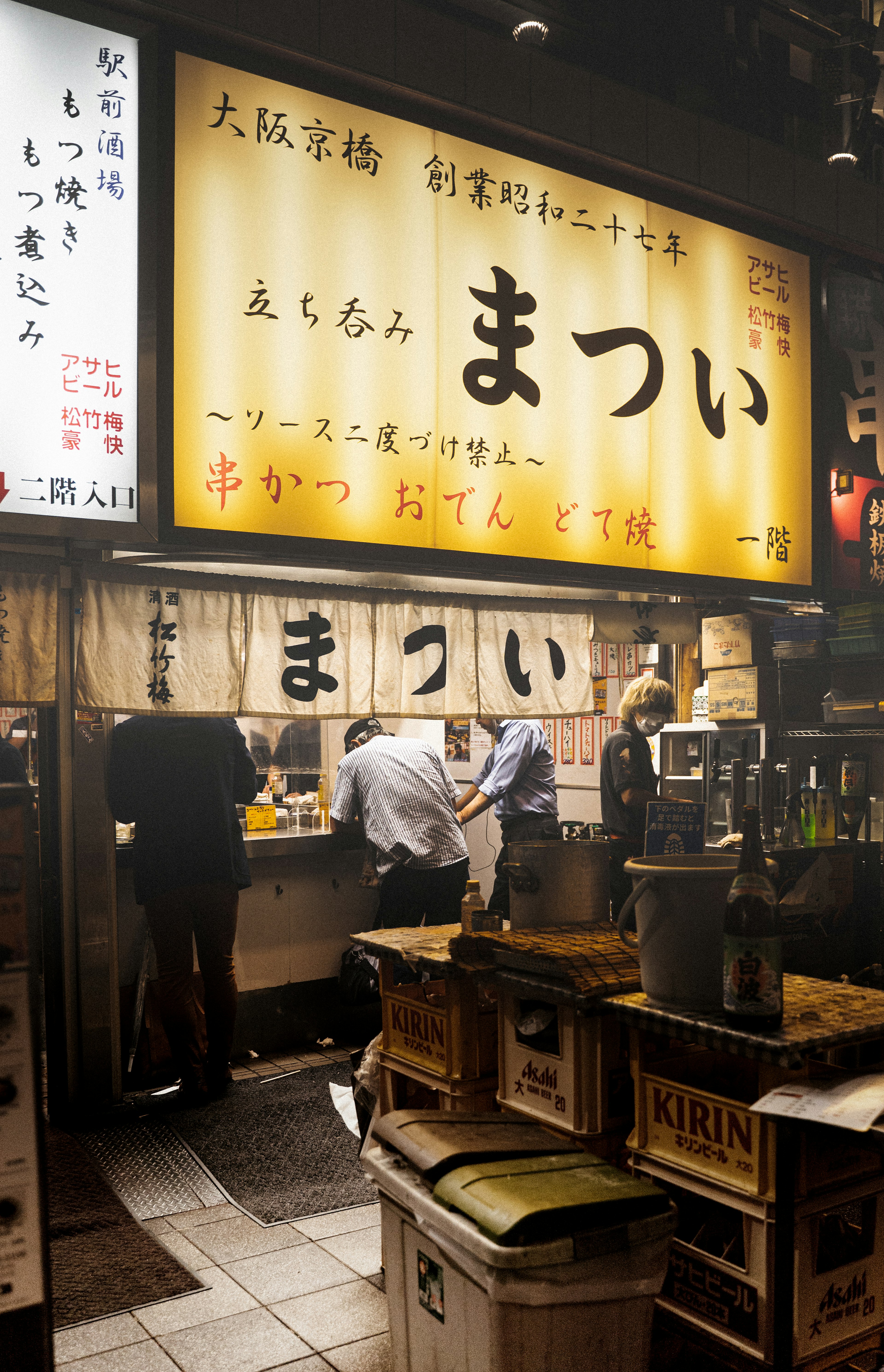 Interior of an Osaka eatery with staff working and a bright sign