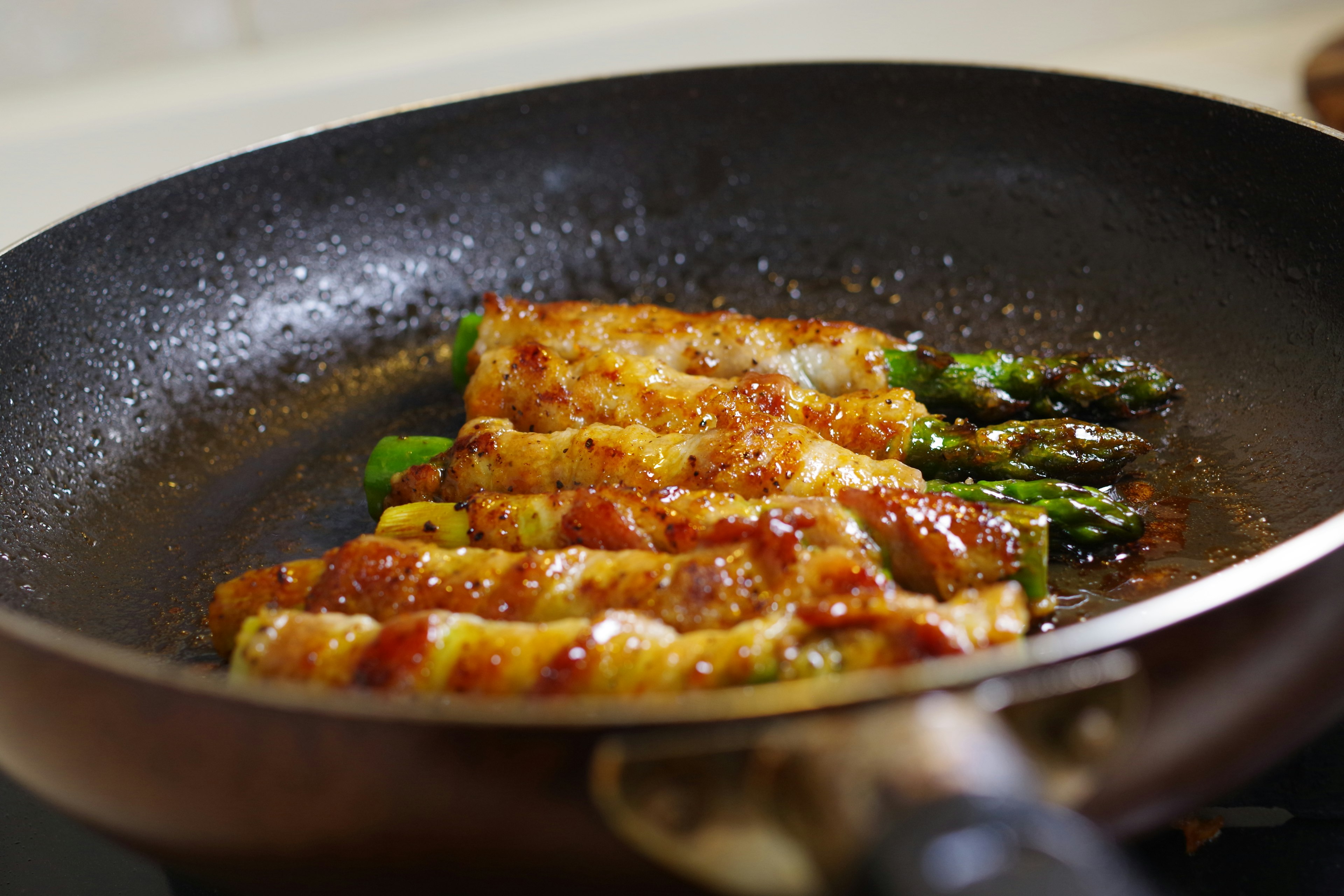 A dish of asparagus and meat rolls cooking in a frying pan