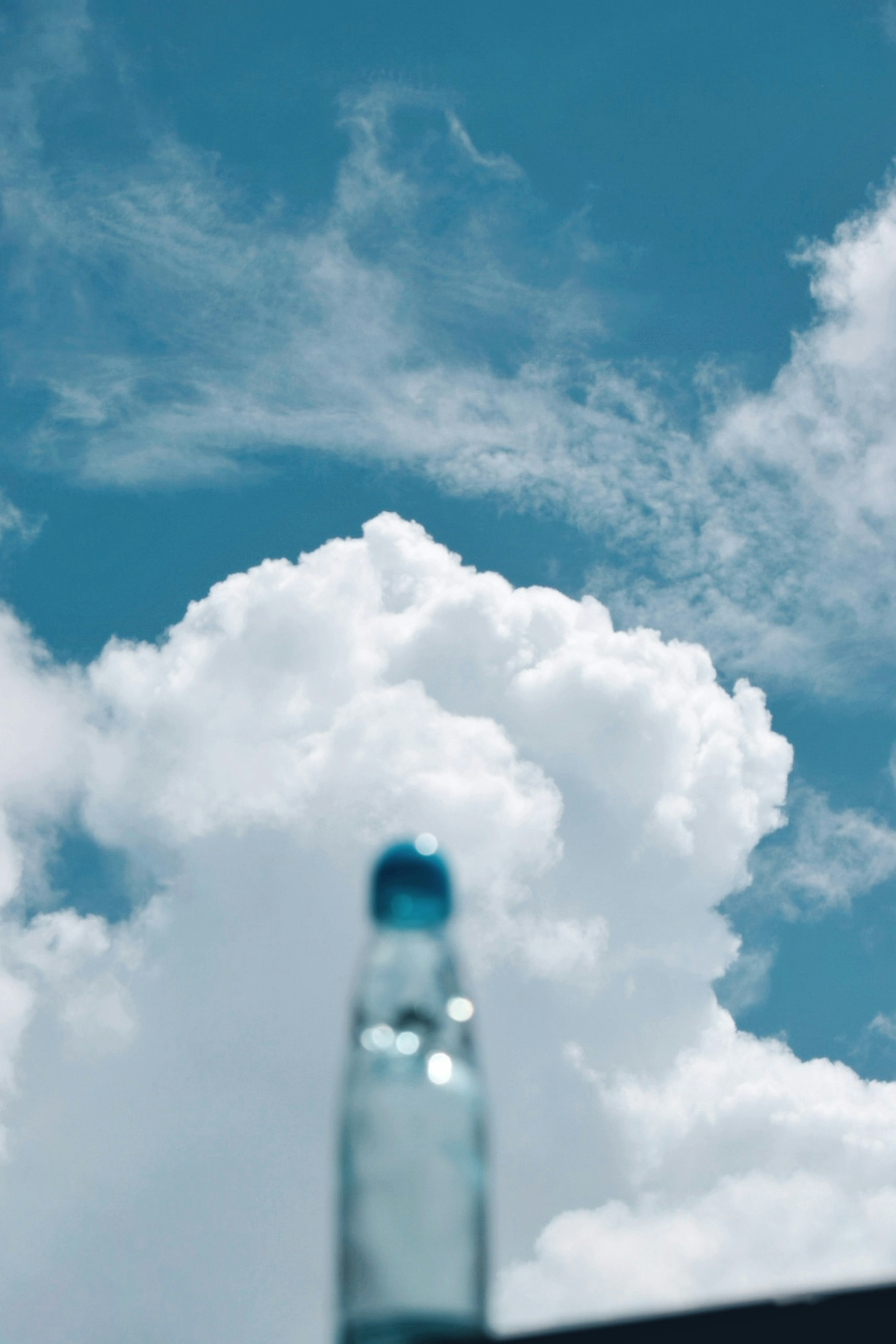 Transparente Flasche vor blauem Himmel und flauschigen weißen Wolken