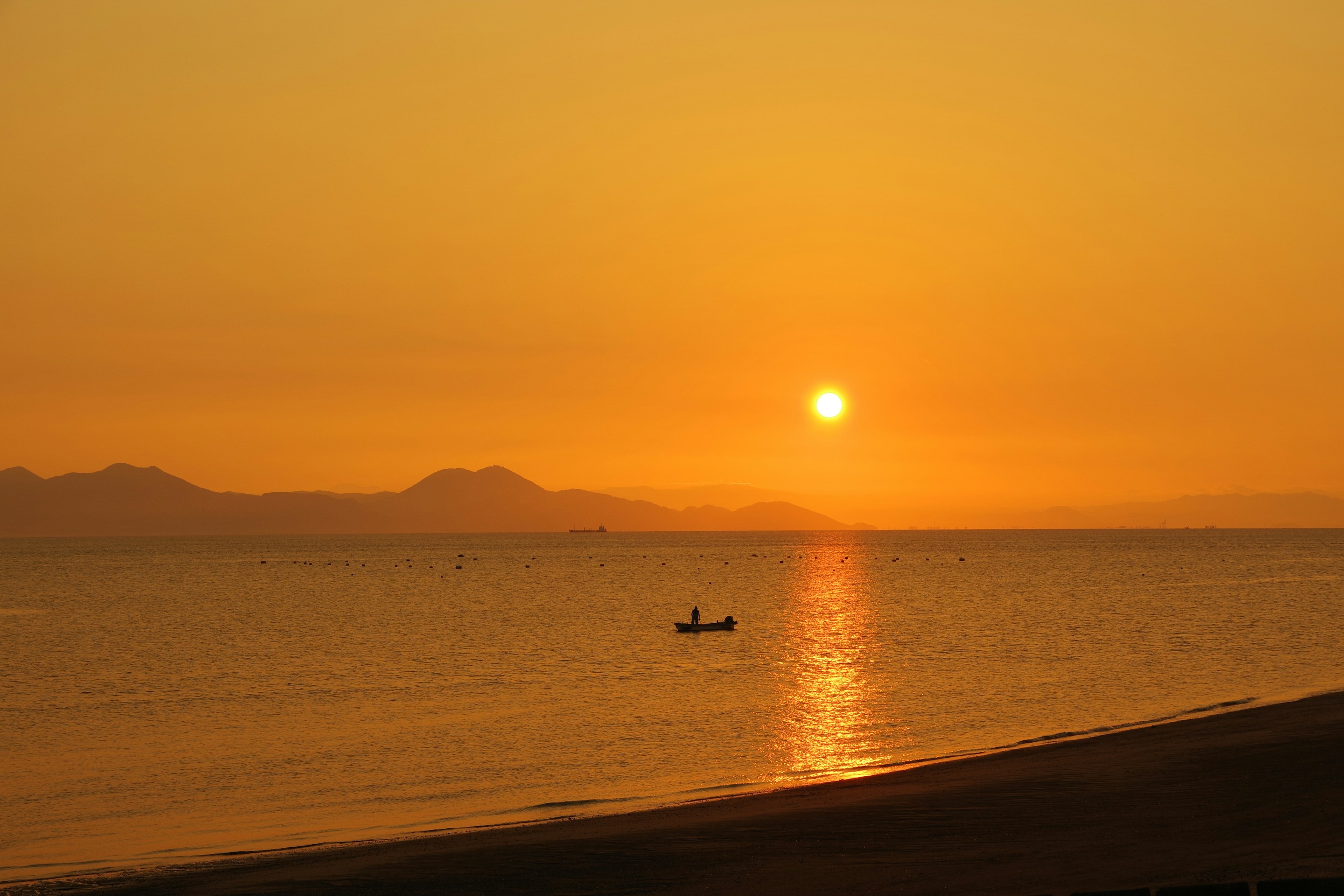 Un hermoso atardecer con un sol naranja hundiéndose en el mar un pequeño bote flotando en silencio