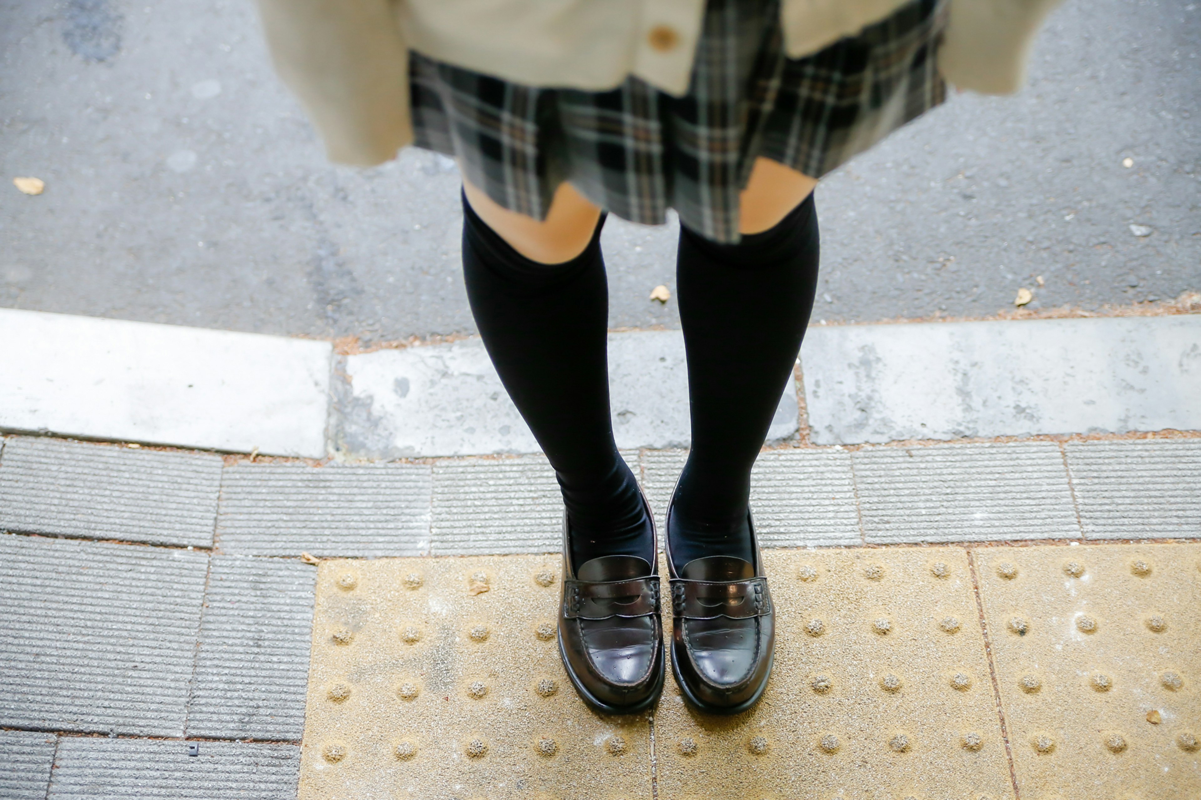 Füße eines Schülers in einem karierten Rock mit schwarzen Socken und Schuhen