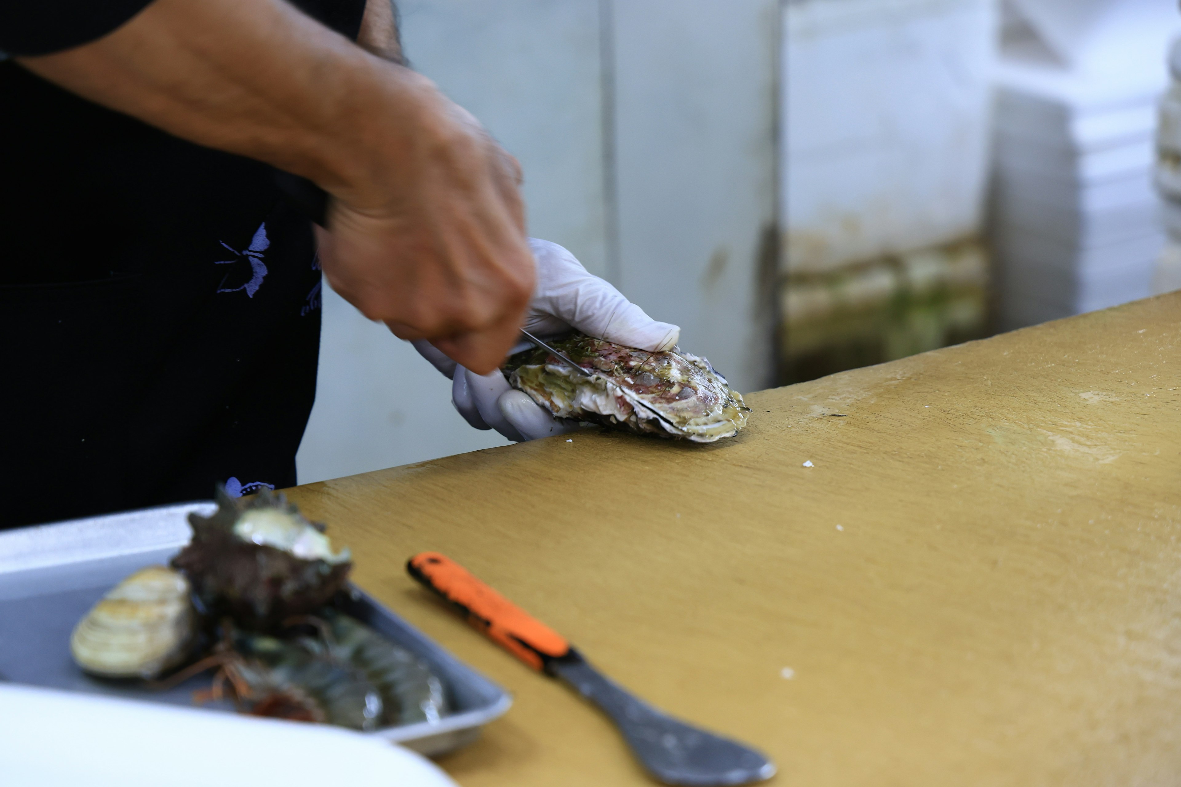 Un chef ouvrant une huître avec un couteau sur un comptoir en bois